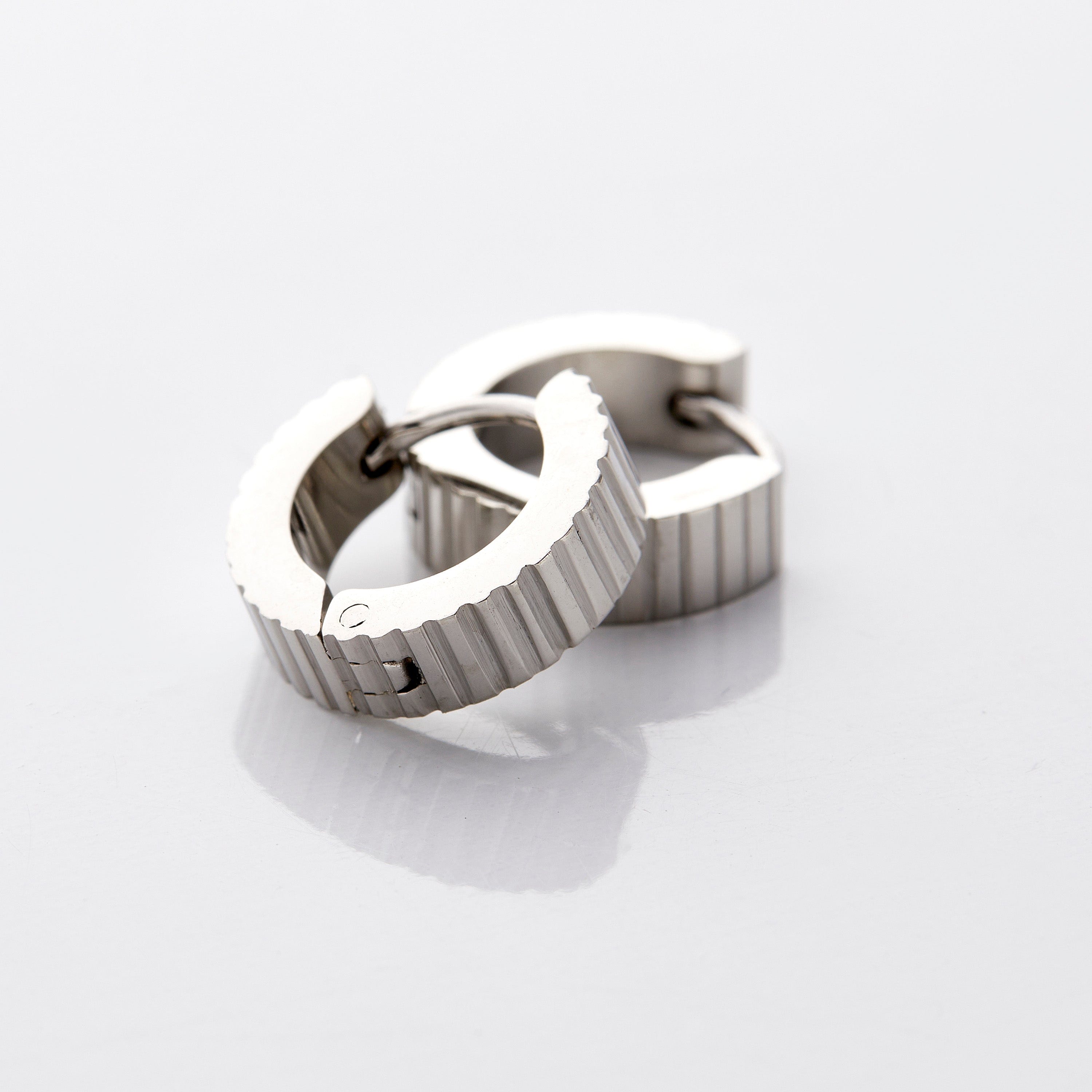 A pair of silver hoop earrings that feature an array of ridges along the outer diameter of these small hugging earrings.