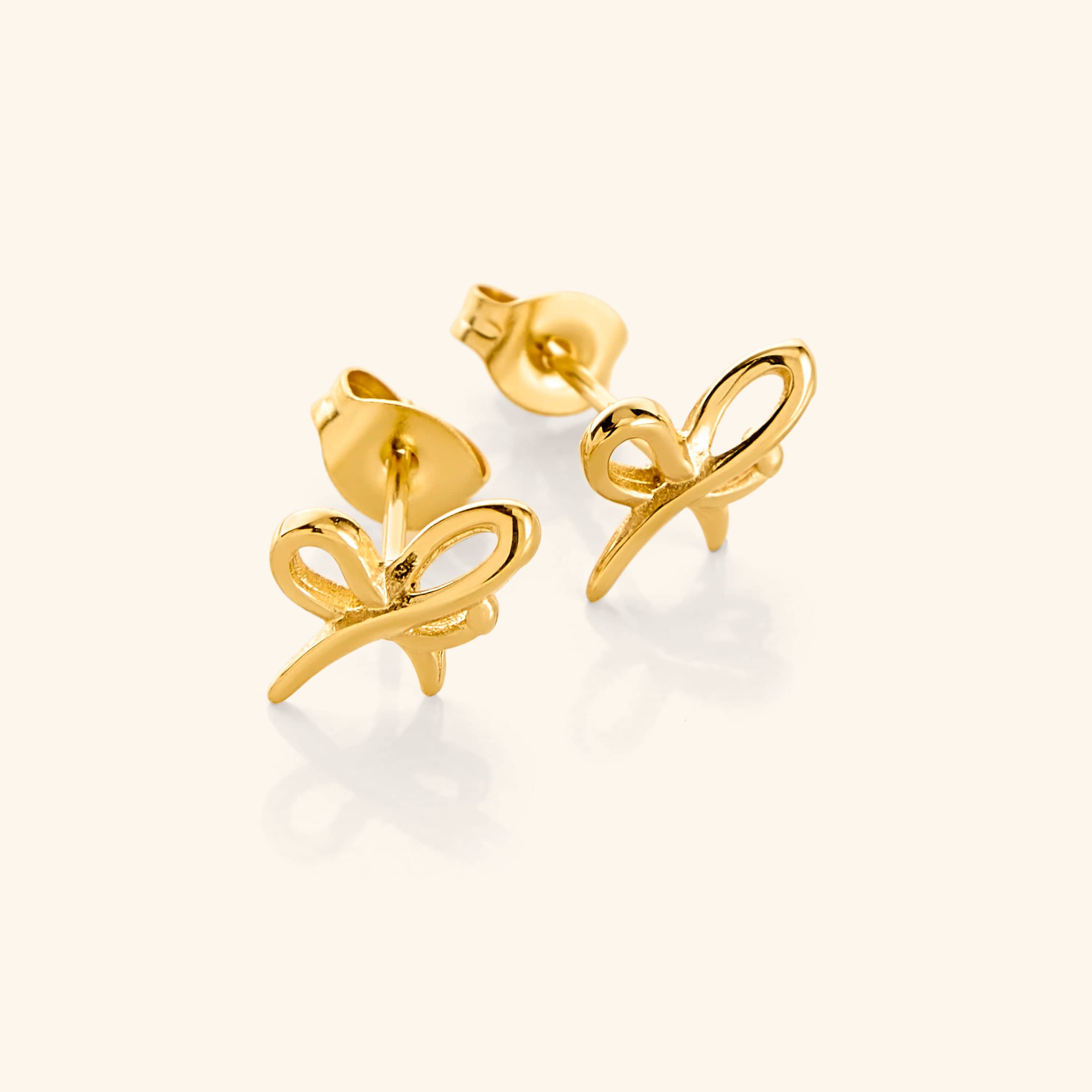 A close-up of the "Mama" Ribbon Studs in 18K gold plating. The earrings feature an elegant ribbon-inspired design, crafted from the Arabic word "ماما" ("Mama"), with the Meem and Alif intertwining to create a bow-like form. The gold finish adds a touch of warmth and sophistication to the studs.