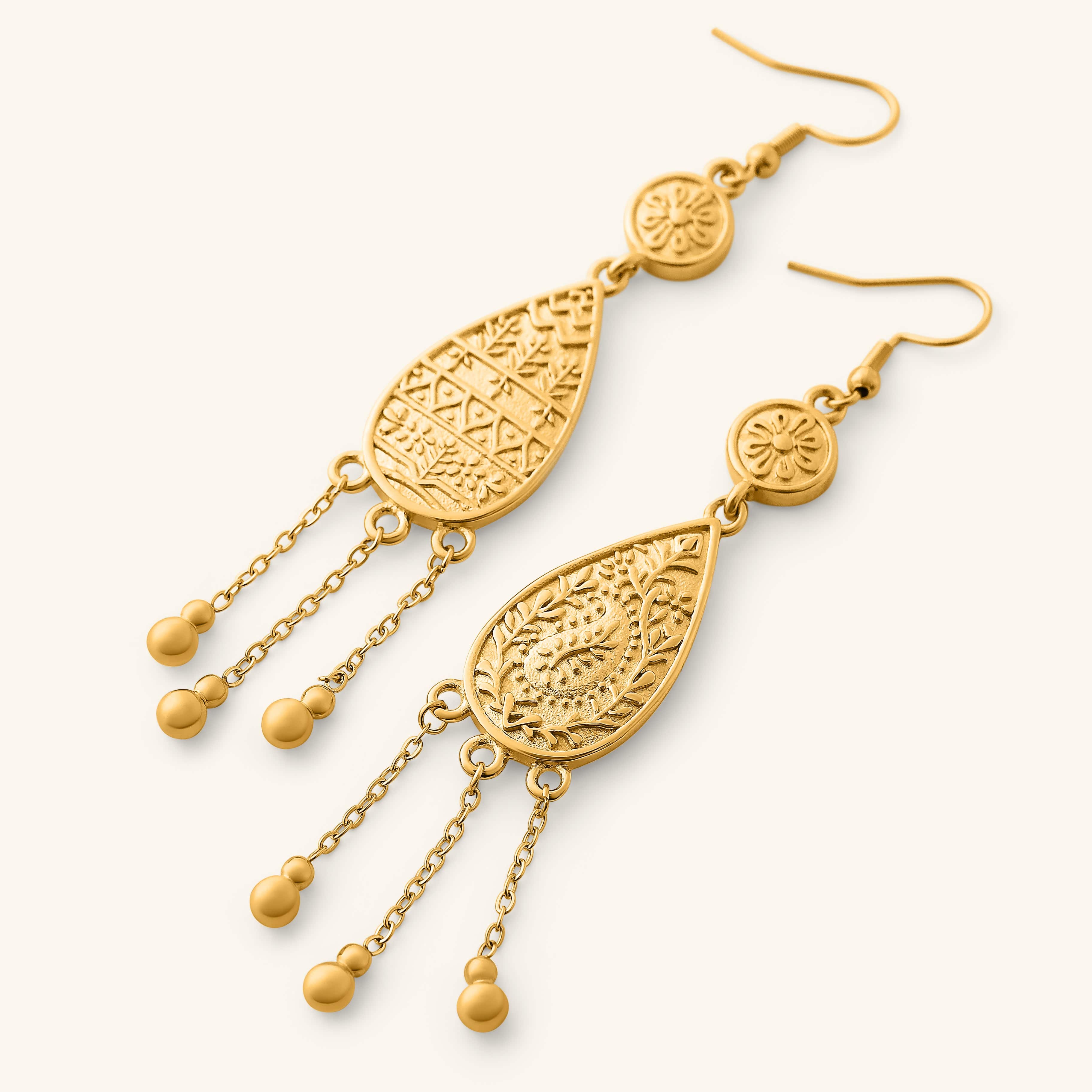 Close-up of the Raining Paisley Earrings, featuring gold teardrop pendants with intricate paisley-inspired patterns and three dangling chains ending in small gold beads.