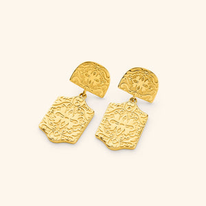 Pair of gold Roaming Earrings featuring intricate engraved patterns on a rounded top piece and a larger dangling rectangular plate with floral and vine motifs, displayed against a light background.
