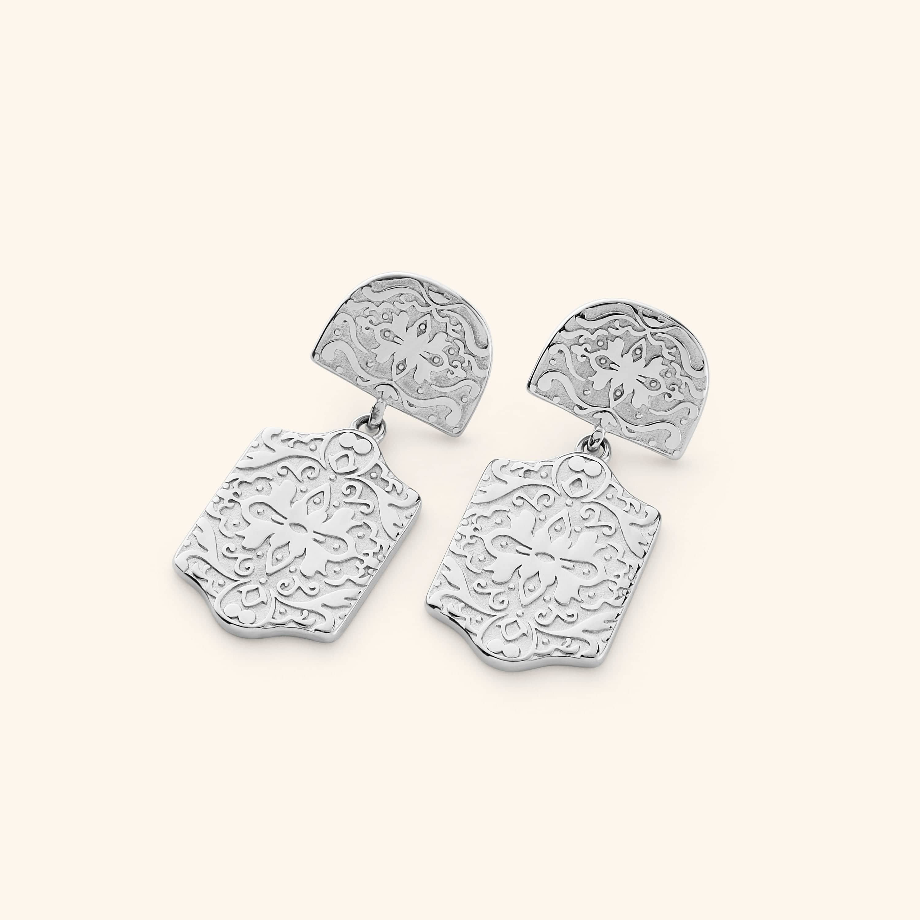 Pair of silver Roaming Earrings featuring engraved floral and vine motifs on both the rounded top and dangling rectangular plates, displayed against a light background.