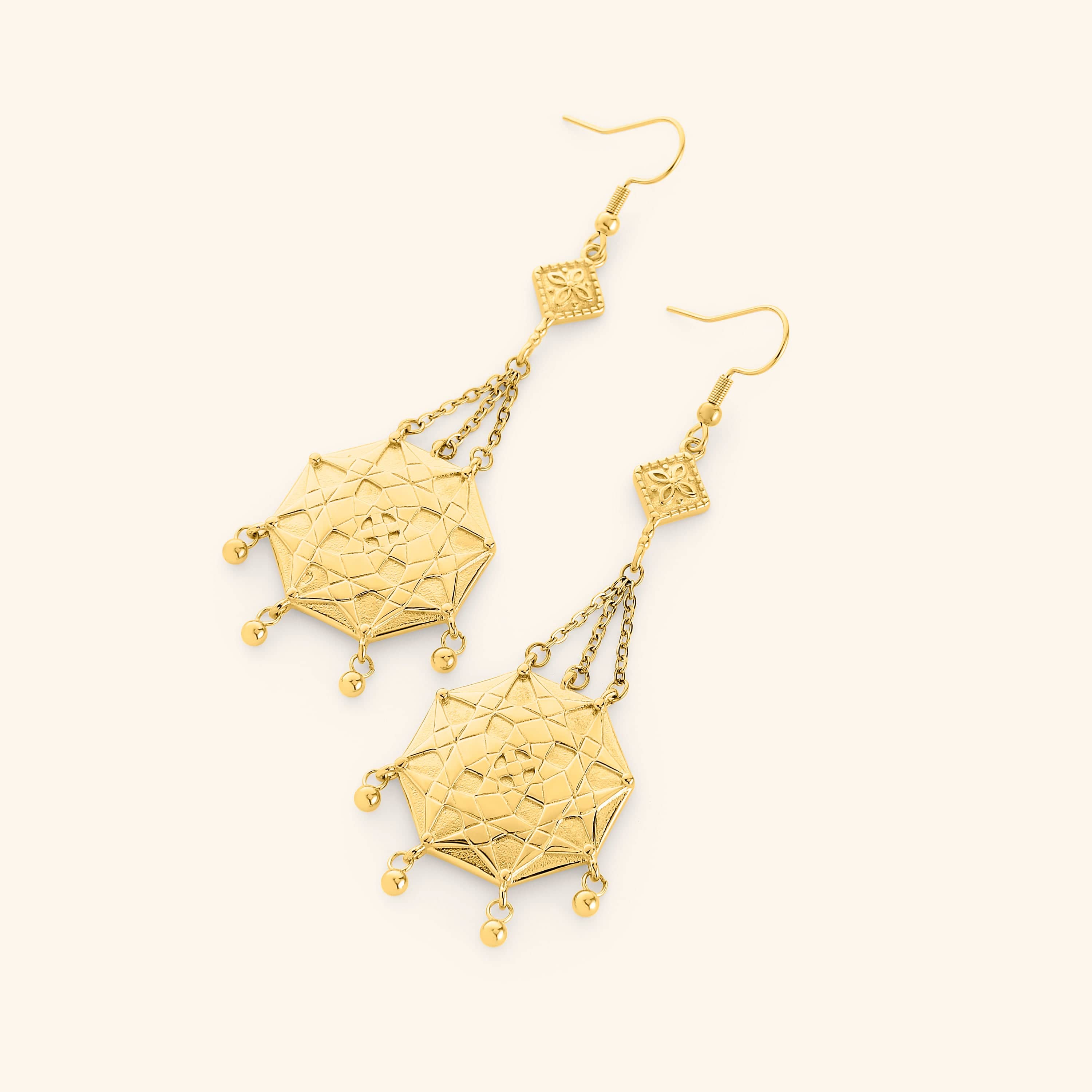 A pair of gold dangling earrings Engraved with the iconic patterns of the mosaic tiles in Syrian homes and fabrics finished with orbs at the bottom of the pendant.