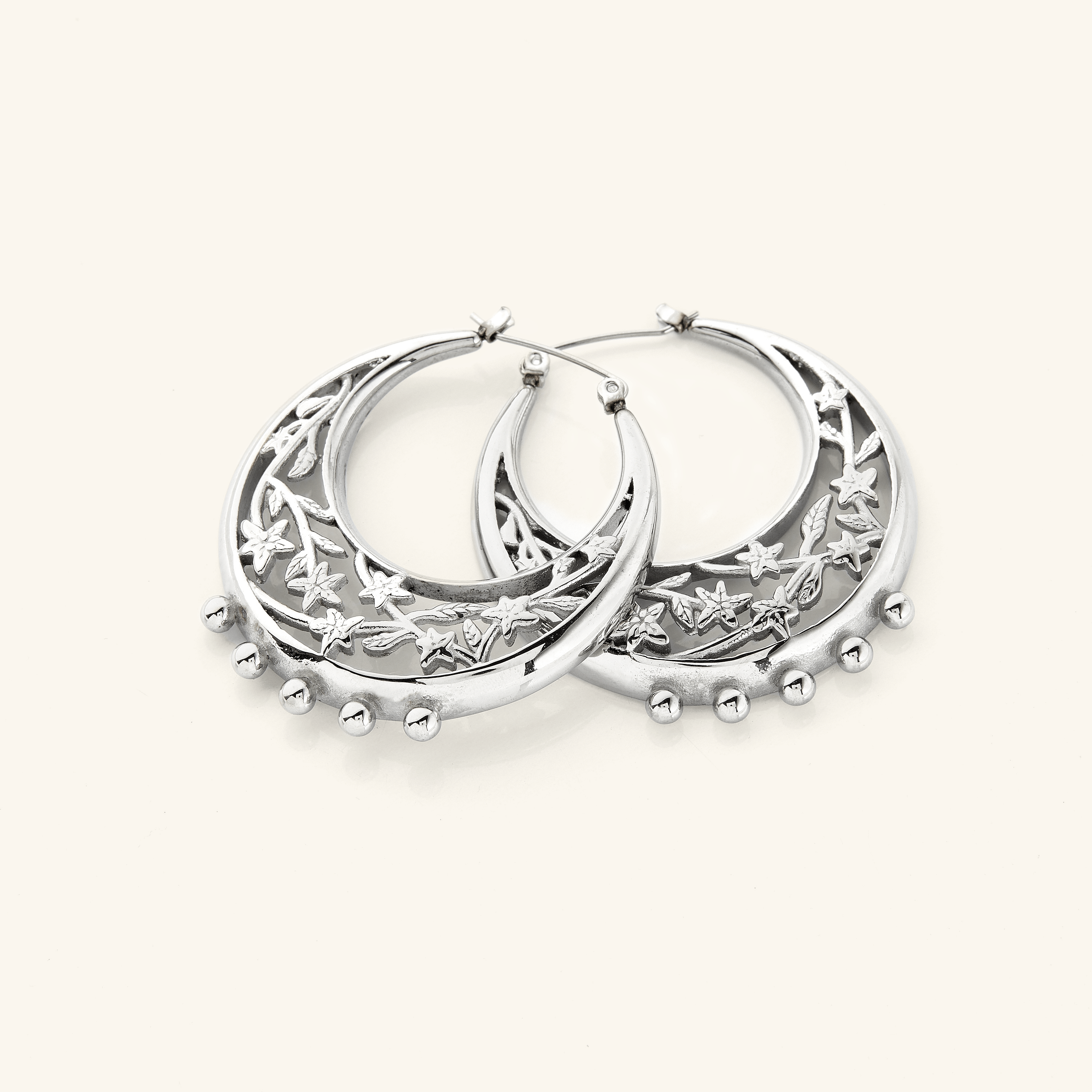 The Jasmine Crescent Hoop Earrings in a polished silver finish, showcasing a chunky hoop design adorned with an intricate jasmine vine that gracefully weaves through the crescent shape, blending celestial inspiration with botanical beauty