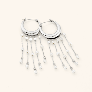 A pair of silver earrings crafted in the shape of a delicate crescent, this hoop gracefully extends to embrace a cascade of raining pearls at its bottom.