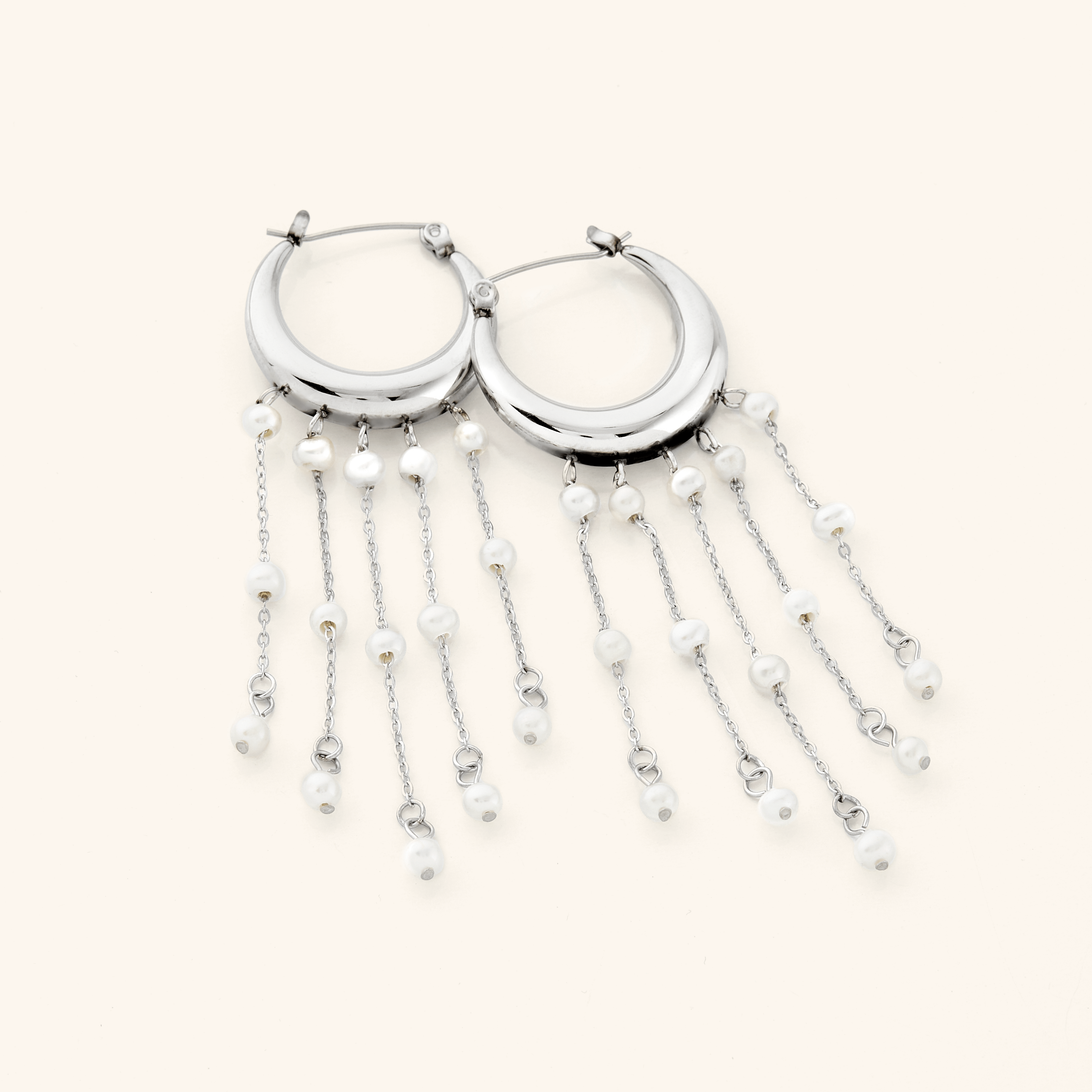 A pair of silver earrings crafted in the shape of a delicate crescent, this hoop gracefully extends to embrace a cascade of raining pearls at its bottom.