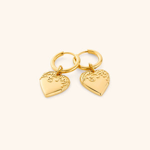 Gold hoop earrings with heart-shaped charm on a white background