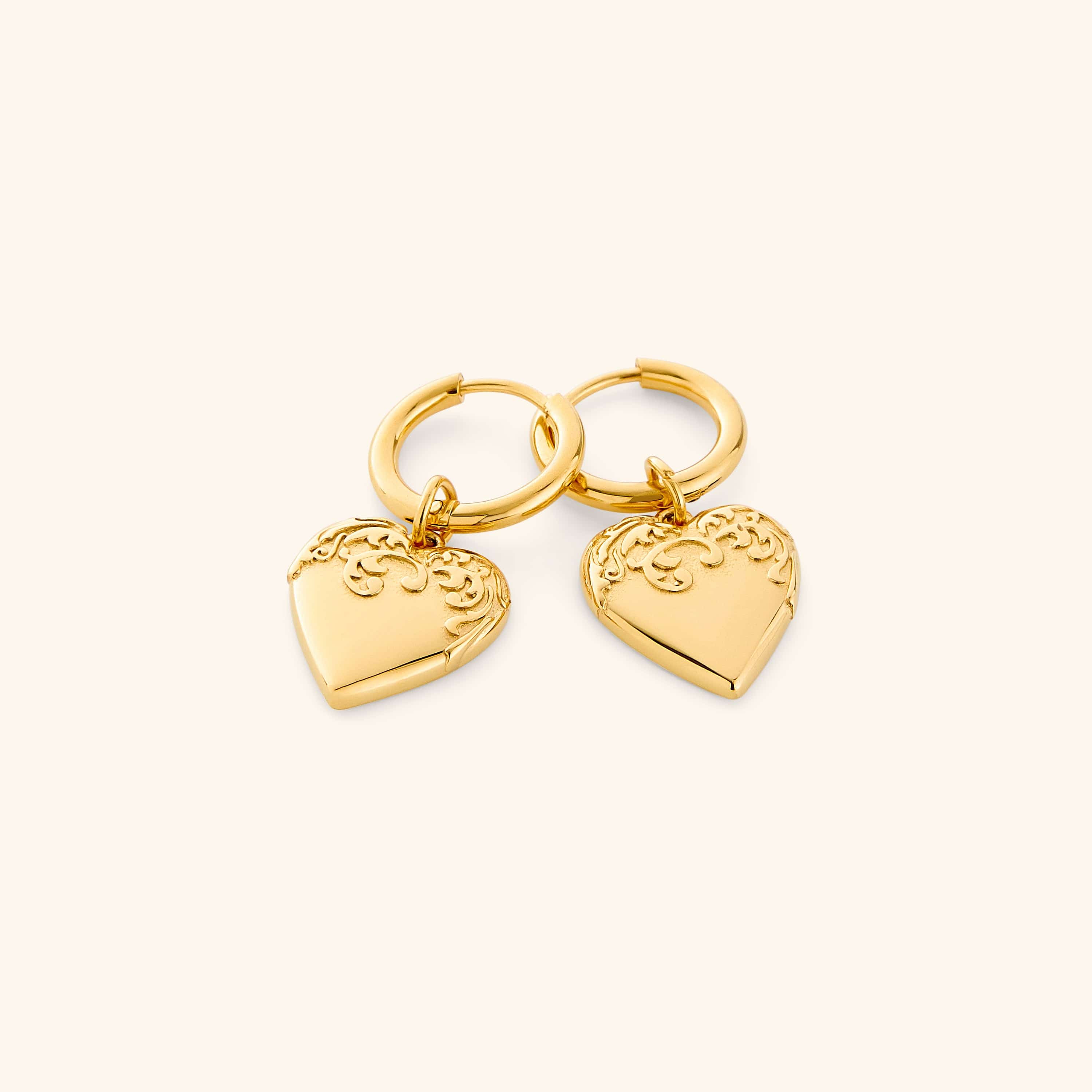 Gold hoop earrings with heart-shaped charm on a white background