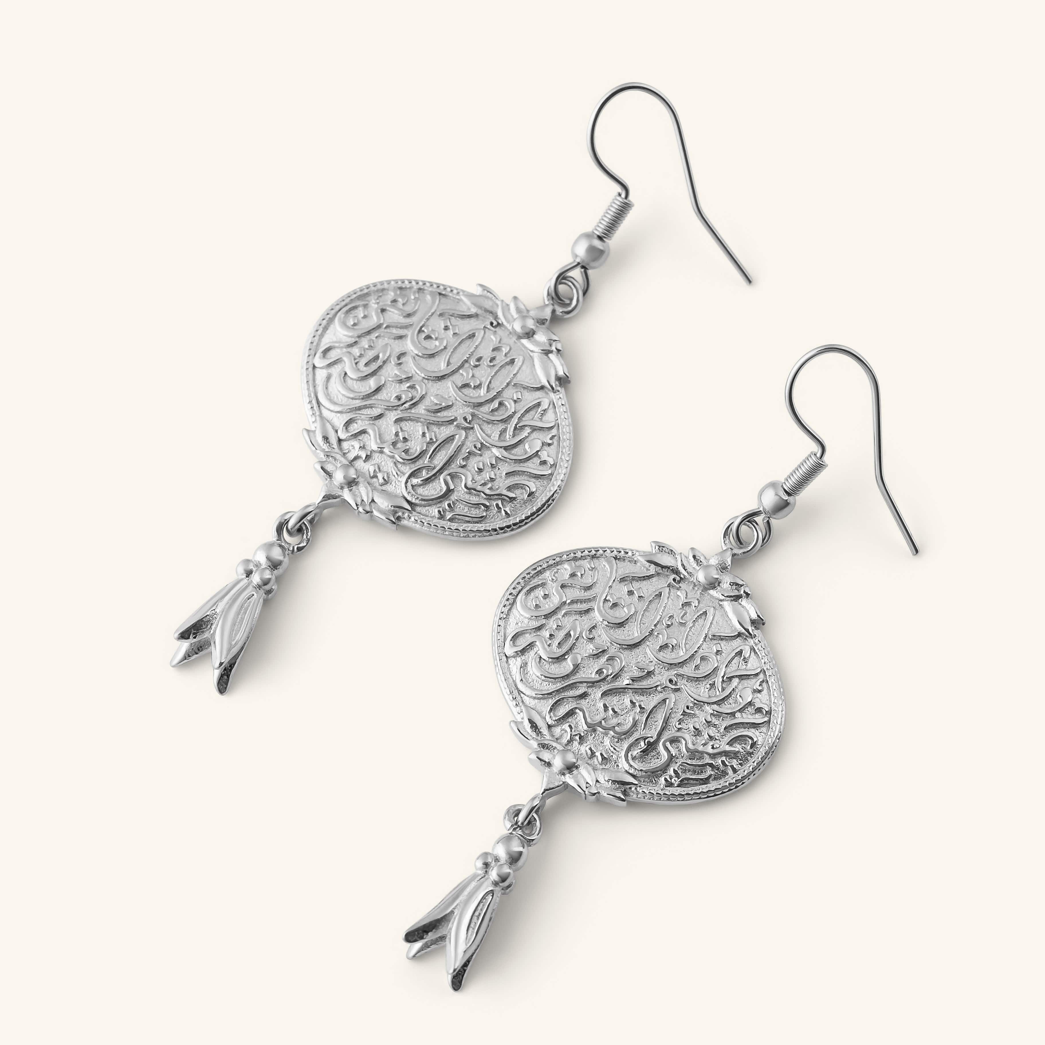 “Walk to Me, and I'll run to you” Medallion Earrings in silver, featuring engraved Arabic calligraphy and a small dangling charm.