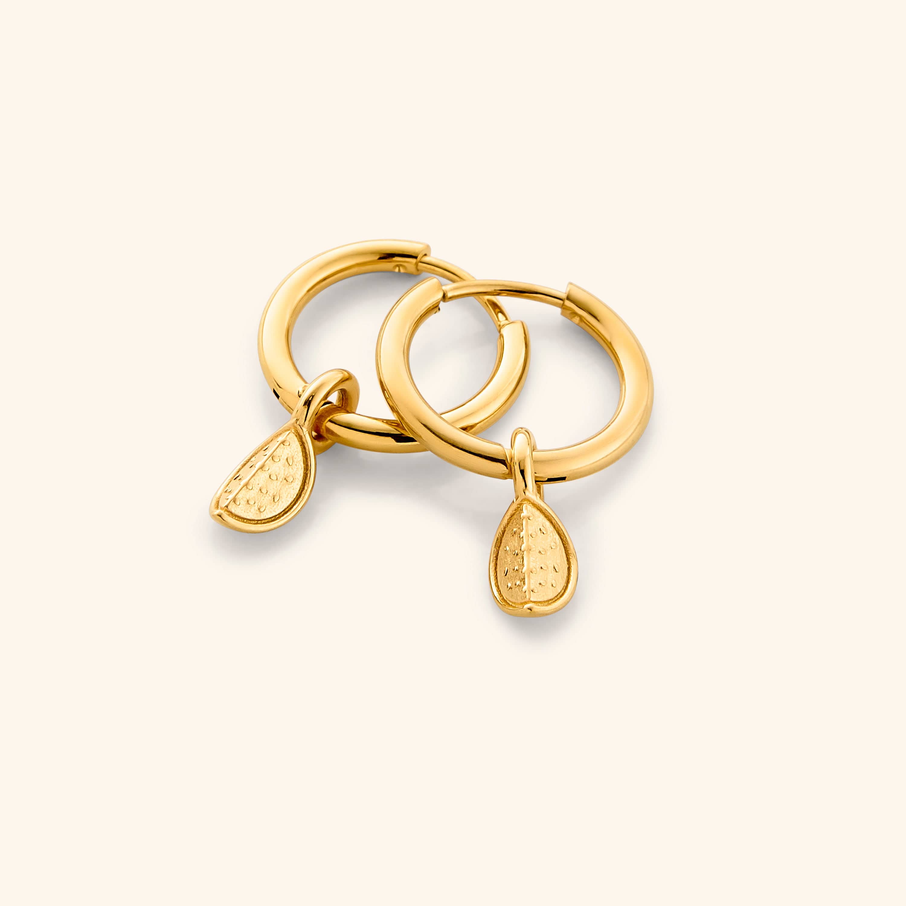 A close-up of the Watermelon Hoops in 18K gold plating. Each earring features a small, semi-circular watermelon slice design with red enamel, black seeds, and green rind detailing, symbolizing the Palestinian flag colors.