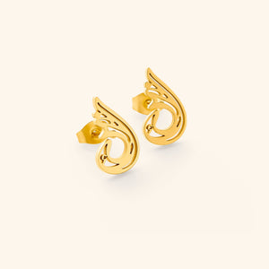 A pair of gold "Serenity Earrings" from the Aadil x Nominal collection. The earrings feature a unique, abstract, teardrop-like design with swirling cut-out details. The metal has a warm gold color. The image is a product shot, likely showcasing the design and craftsmanship of the earrings.