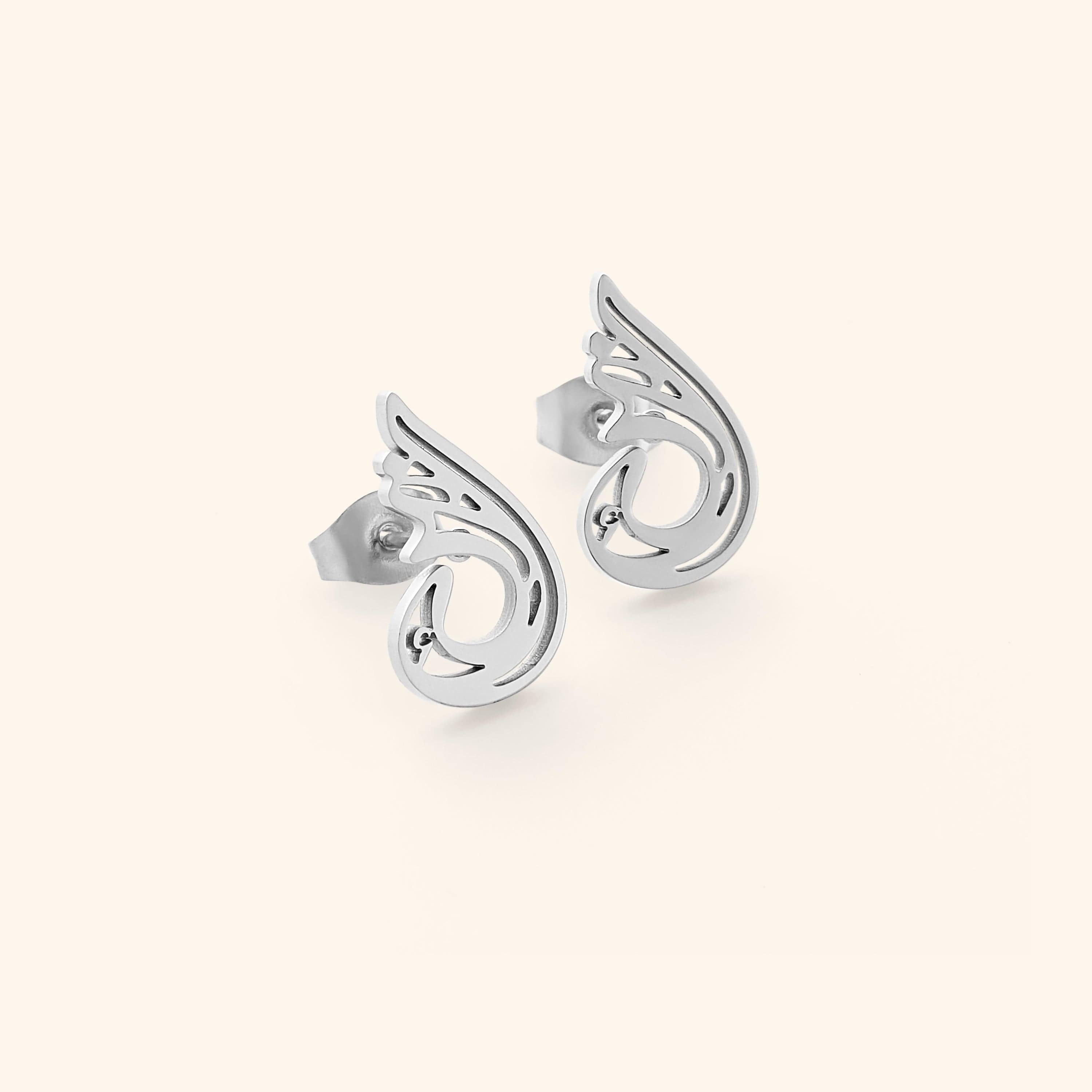 A pair of silver "Serenity Earrings" from the Aadil x Nominal collection. The earrings feature a unique, abstract, teardrop-like design with swirling cut-out details. The image is a product shot, likely showcasing the design and craftsmanship of the earrings.