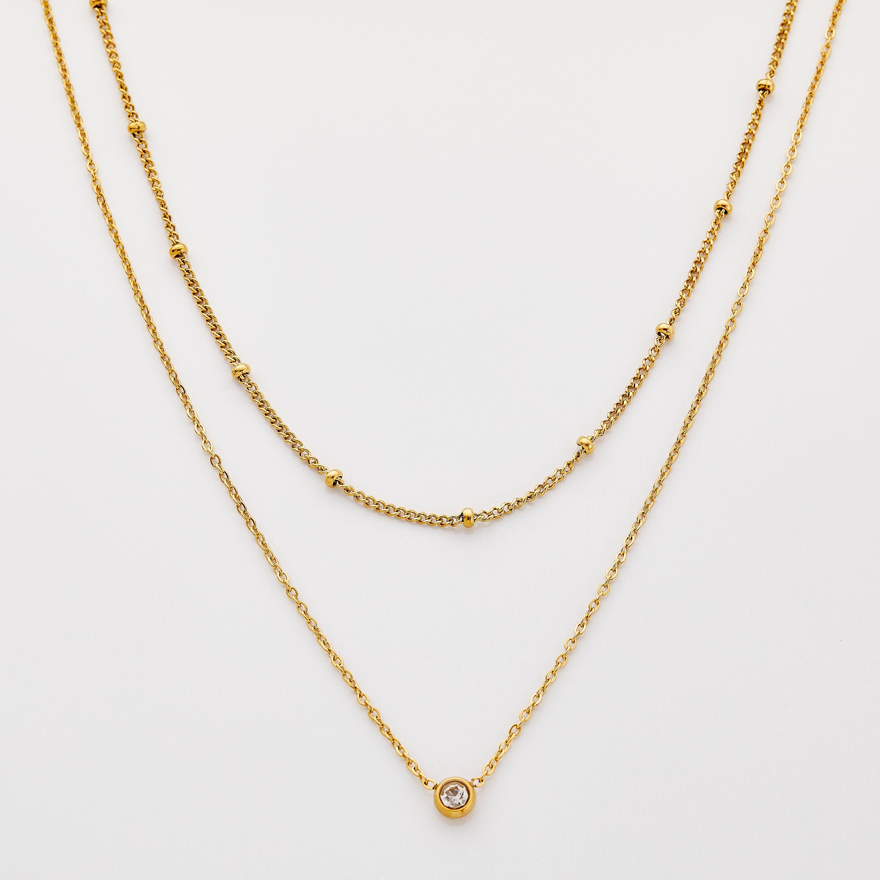 Gold necklace set featuring a bead-accented chain layered with a solitaire bezel-set pendant necklace.