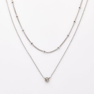 Silver necklace set featuring a bead-accented chain layered with a solitaire bezel-set pendant necklace.