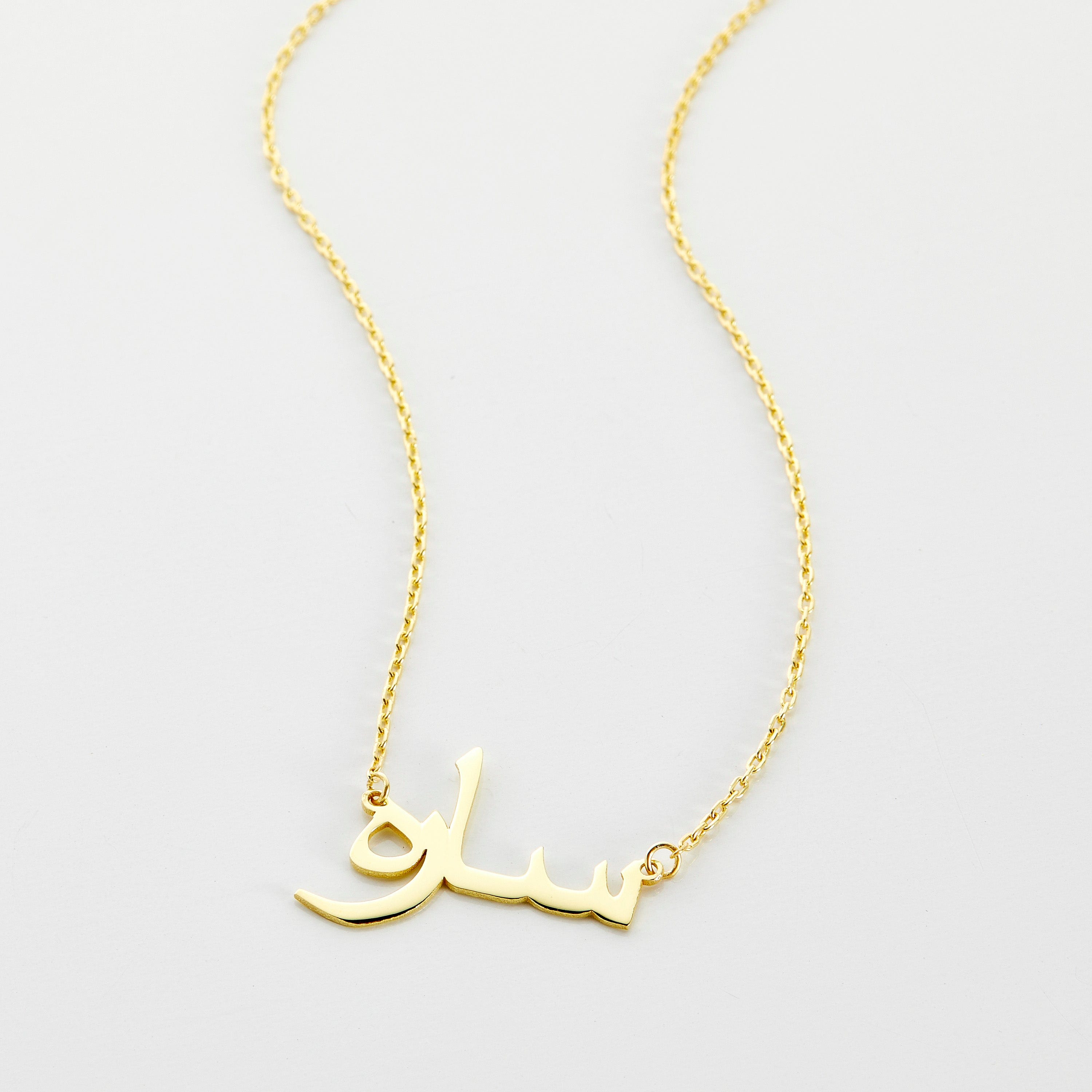 A close-up of the Custom Name Necklace in 14K solid gold, featuring the Arabic name "ساره" ("Sarah") in elegant calligraphy. The pendant is suspended from a delicate gold chain, highlighting the craftsmanship and personalized design.