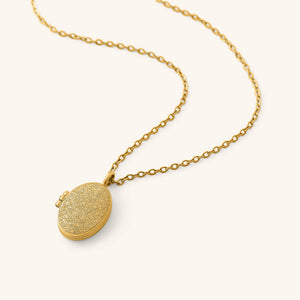 Gold oval locket engraved with detailed Ayatul Kursi calligraphy on the front, hanging from a gold chain on a neutral background.