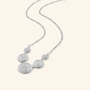 Silver necklace featuring a chain that is strung with coins stamped with الحمد لله (all praise is due to God). Gold coins are layered at varying sizes so they sit asymmetrically