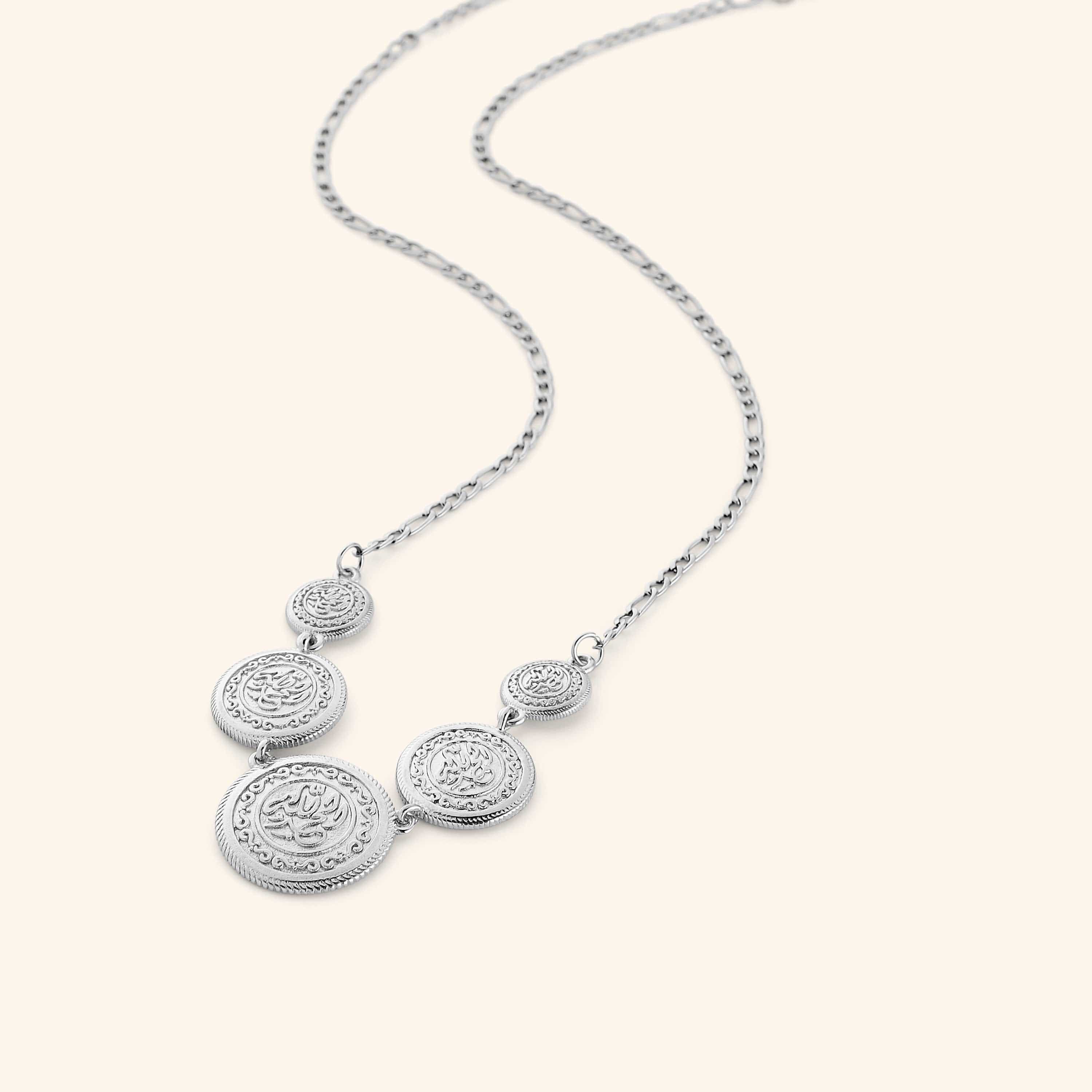Silver necklace featuring a chain that is strung with coins stamped with الحمد لله (all praise is due to God). Gold coins are layered at varying sizes so they sit asymmetrically