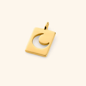 Gold rectangular charm with a crescent moon cutout, resting flat on a cream background with a soft shadow.