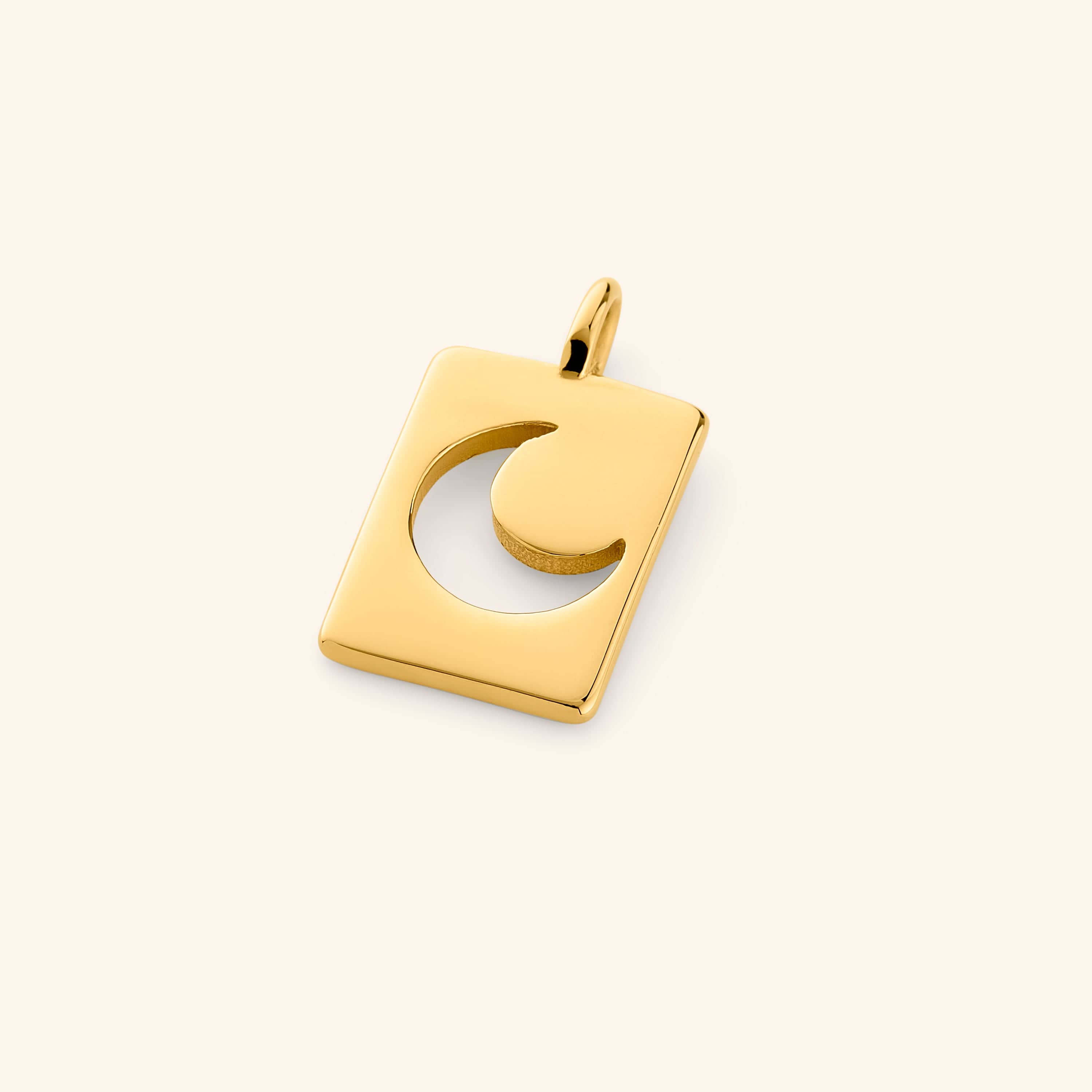 Gold rectangular charm with a crescent moon cutout, resting flat on a cream background with a soft shadow.