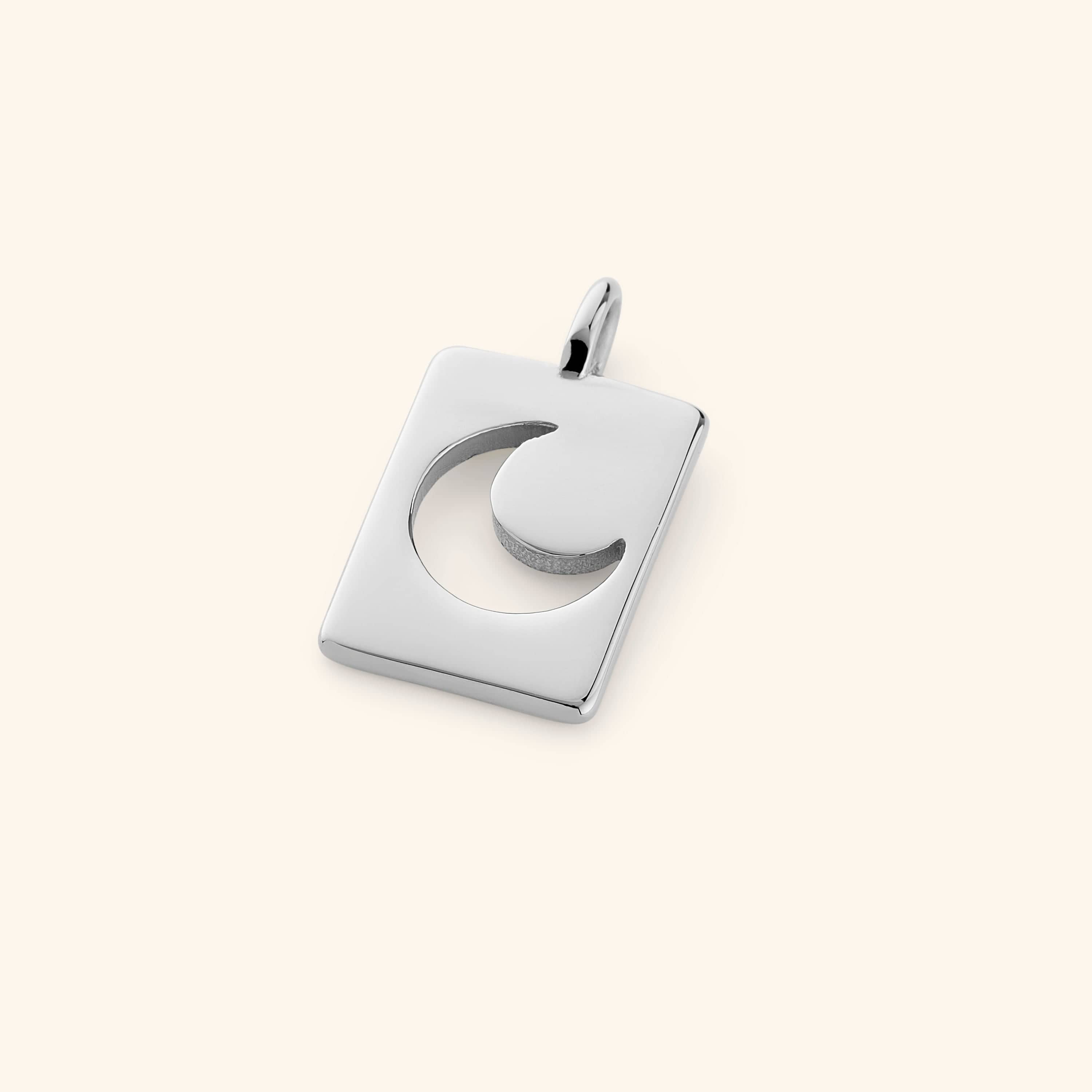 Silver version of the rectangular crescent charm, displayed flat on a cream background, with soft reflections along its edges.
