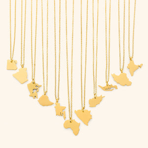 The image shows a collection of delicate gold necklaces hanging vertically against a light beige background. Each necklace features a flat, polished gold pendant shaped like the outline of a different country or region.
