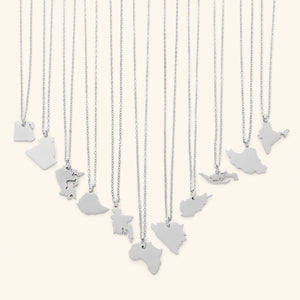 The image shows a collection of delicate silver necklaces hanging vertically against a light beige background. Each necklace features a flat, polished silver pendant shaped like the outline of a different country or region.