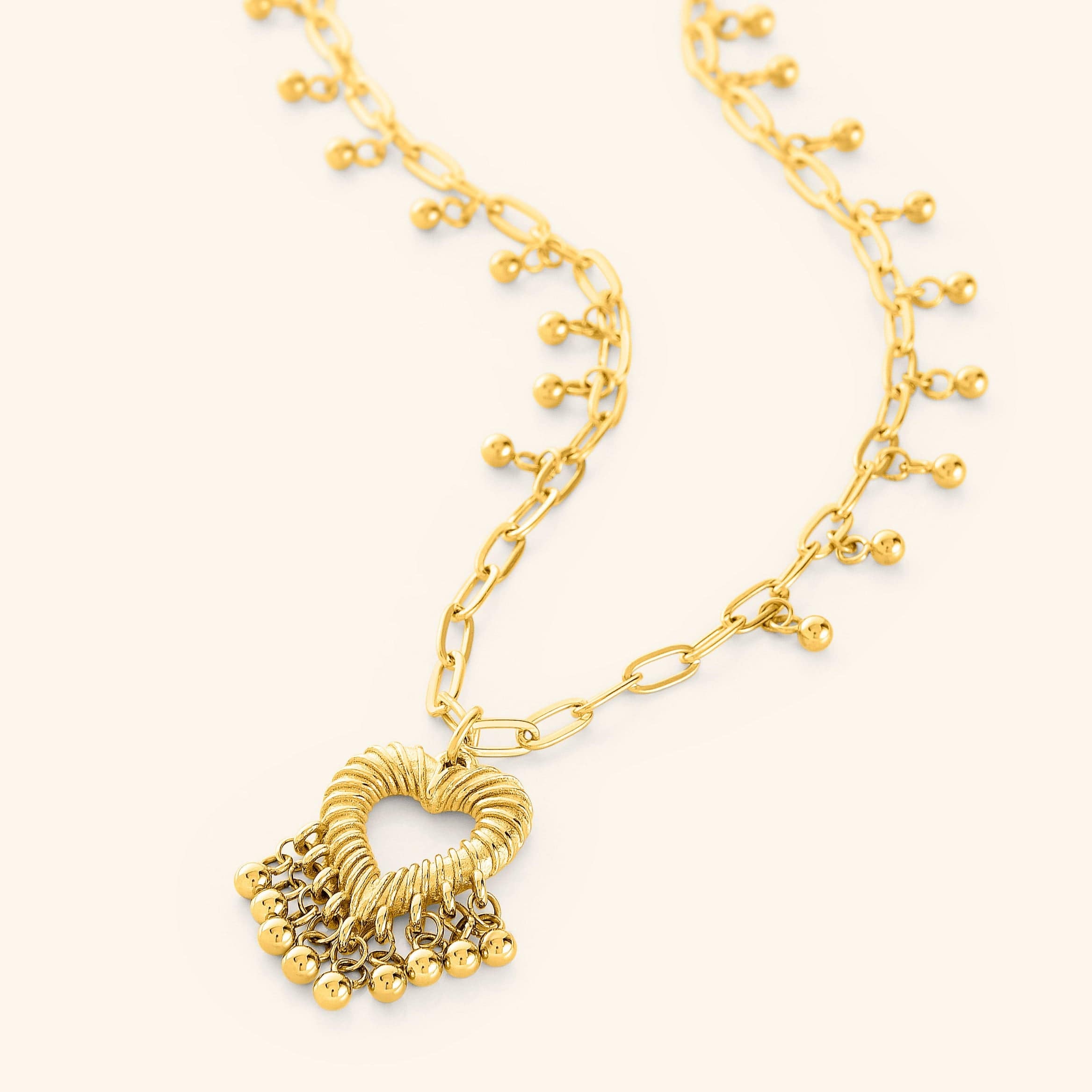 A gold-plated necklace featuring a heart-shaped pendant with three small dangling orbs, displayed on a white background.