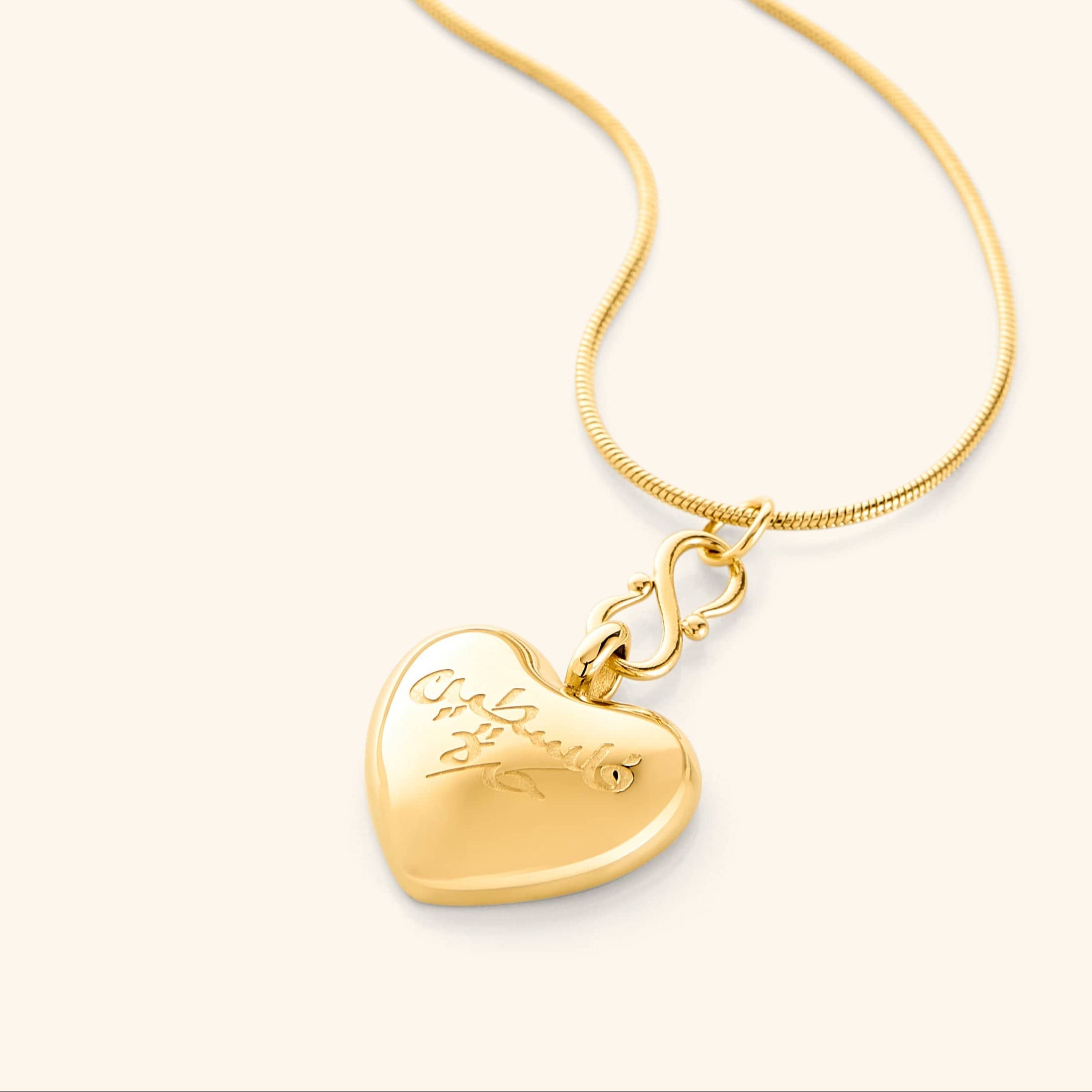 Photo of an 18k gold plated thin chain necklace that features a  puffed heart pendant is engraved with the words “Free Palestine” in Arabic (فلسطين حرة).