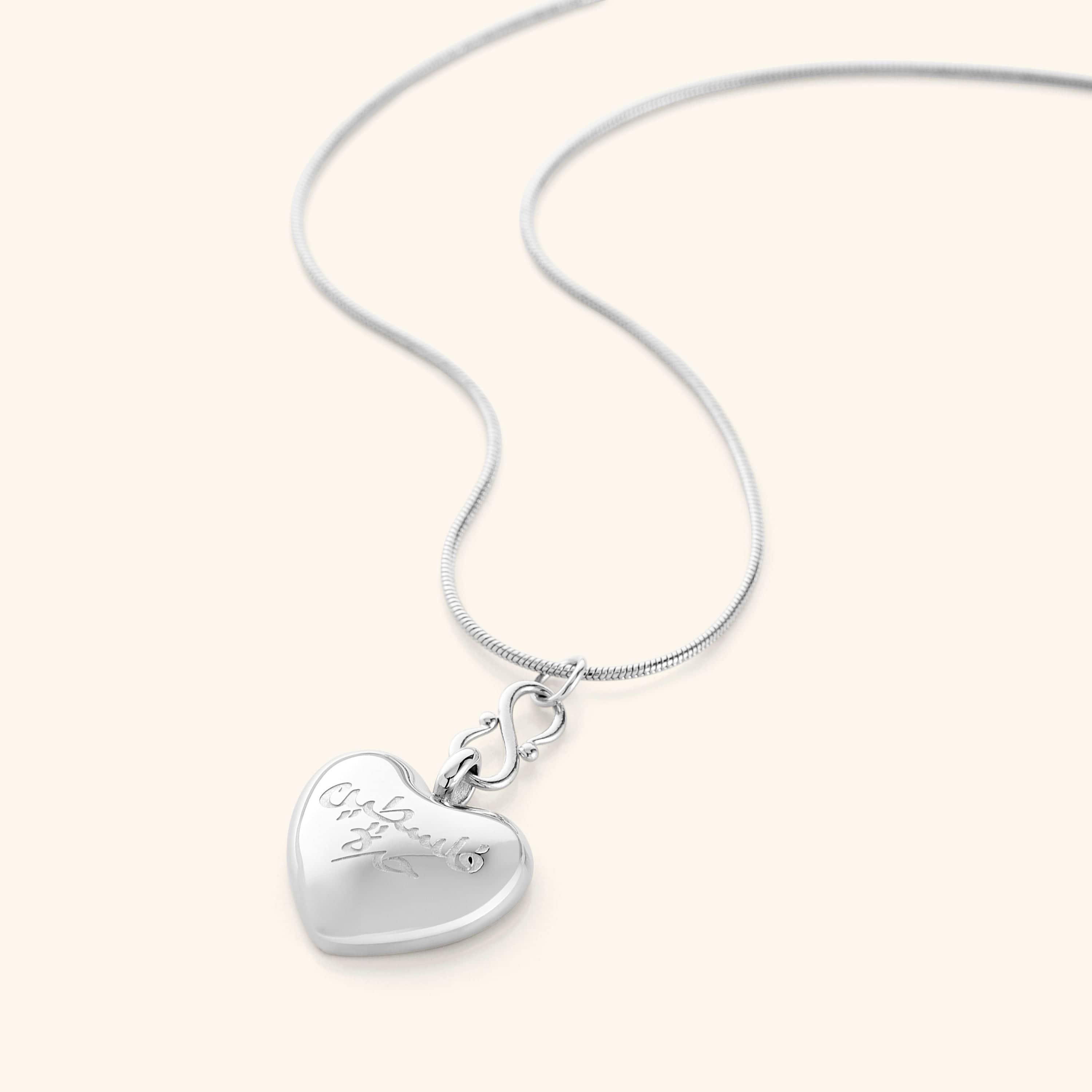 Photo of a silver thin chain necklace that features a  puffed heart pendant is engraved with the words “Free Palestine” in Arabic (فلسطين حرة).