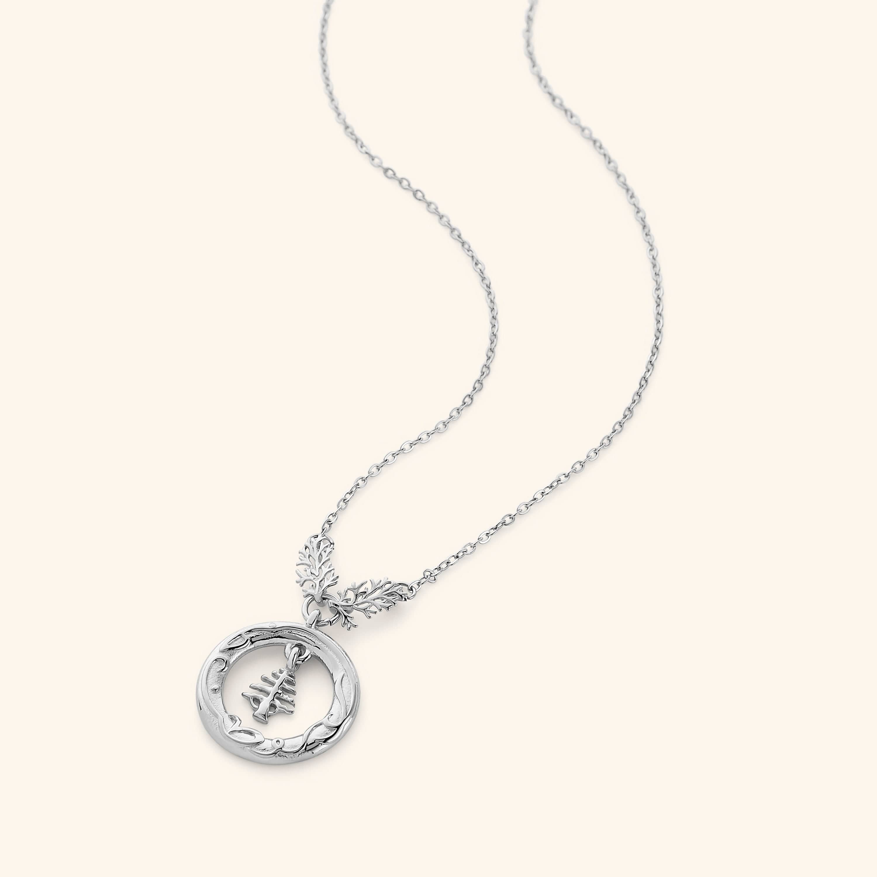 Silver necklace features the Lebanon Cedar tree suspended in a disc that is embossed with "love of the homeland" around the perimeter hanging on a thin gold chain.