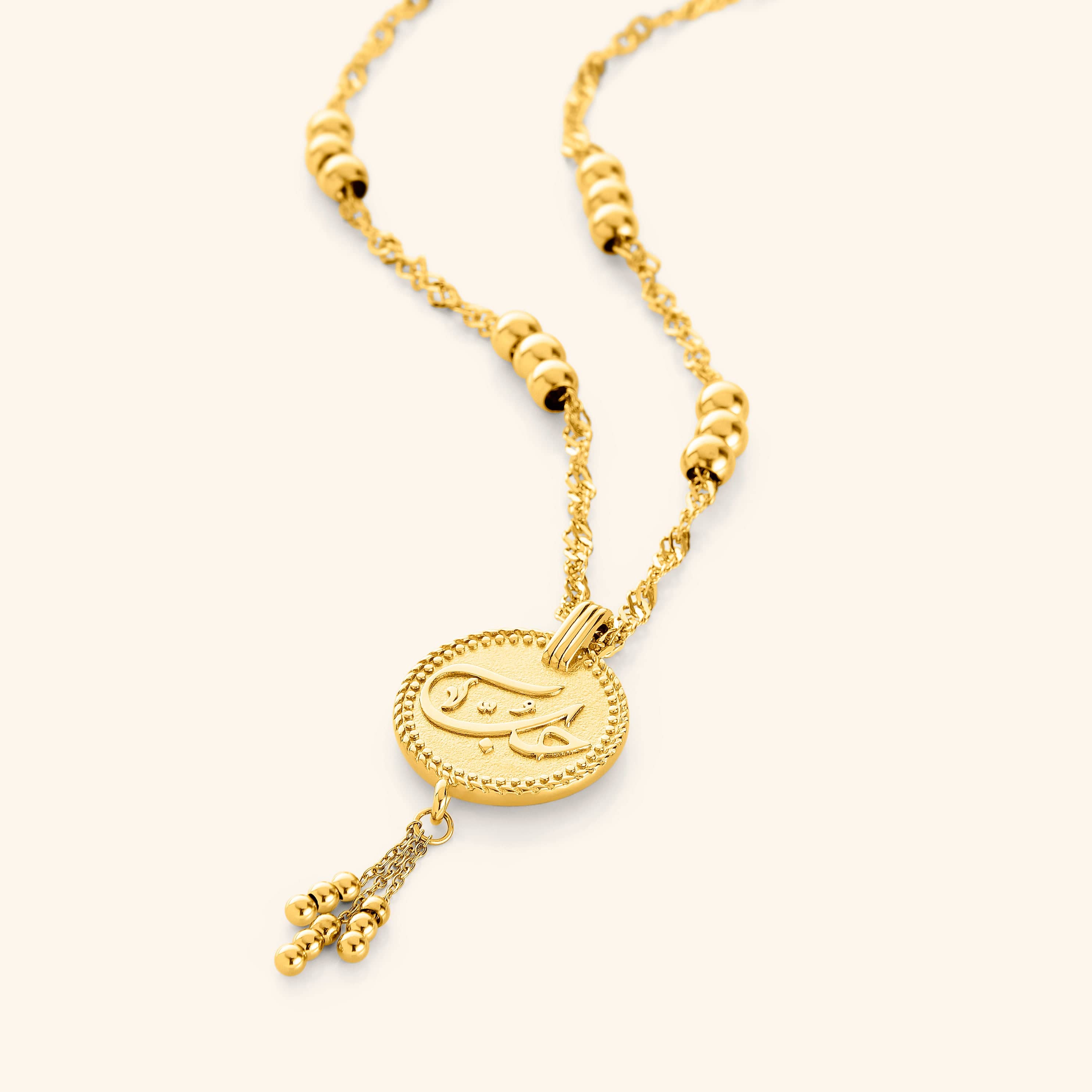 Flat lay of an 18k gold plated necklace that features Love, حب, etched in Arabic, designed with vintage coin jewelry in mind, this piece is adorned with delicate dangling orbs.