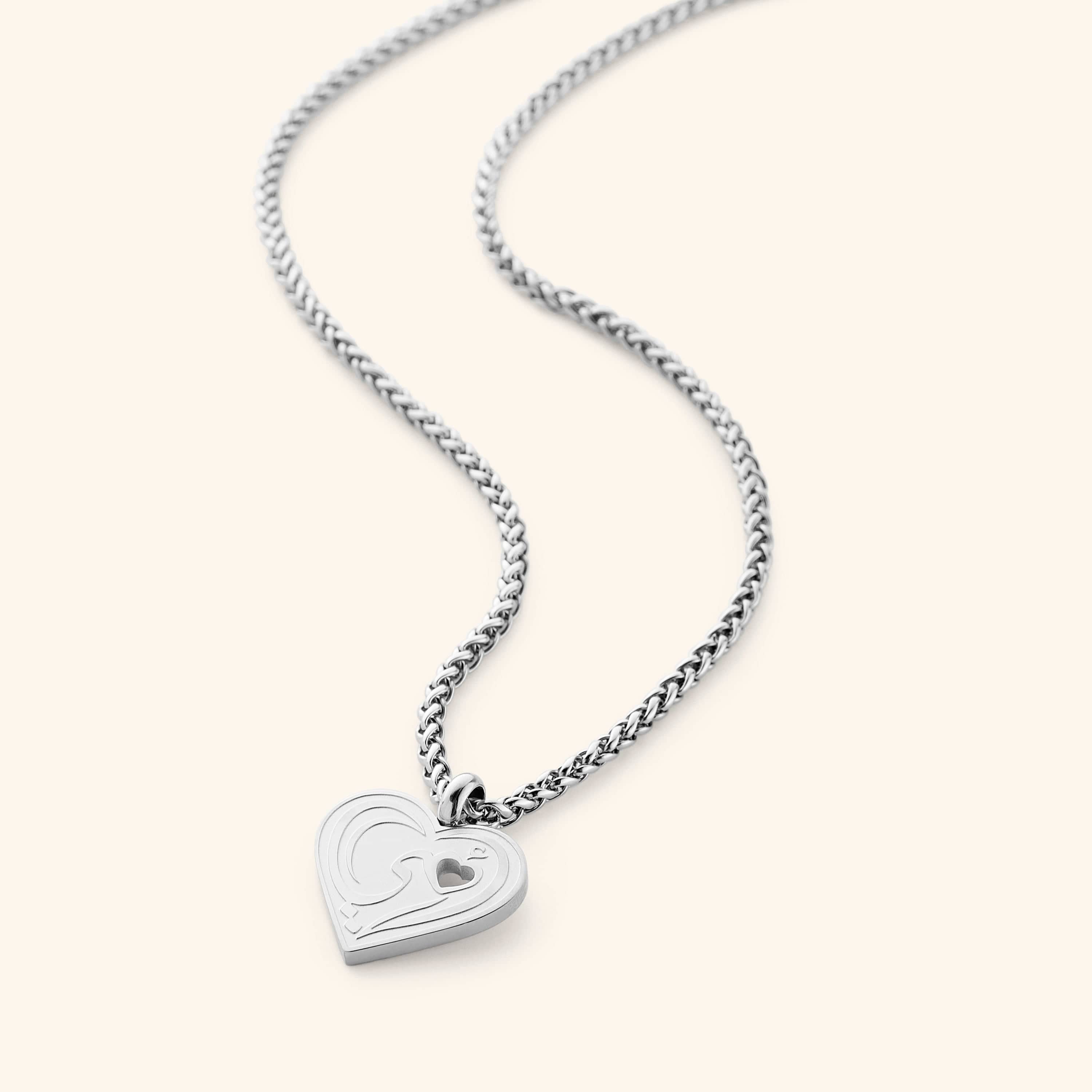 The "Piece of Me" Mama Necklace in a polished silver finish, showcasing a heart-shaped pendant with the Arabic inscription "Ummi" and a tiny heart-shaped cutout, suspended from a sleek wheat chain.