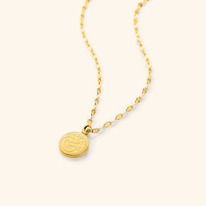 A close-up of the My Mother Necklace in 18K gold plating. The round pendant features the Arabic word "أمي" ("Ummi" – My Mother) engraved in elegant calligraphy, suspended from a delicate gold Flutter Chain.