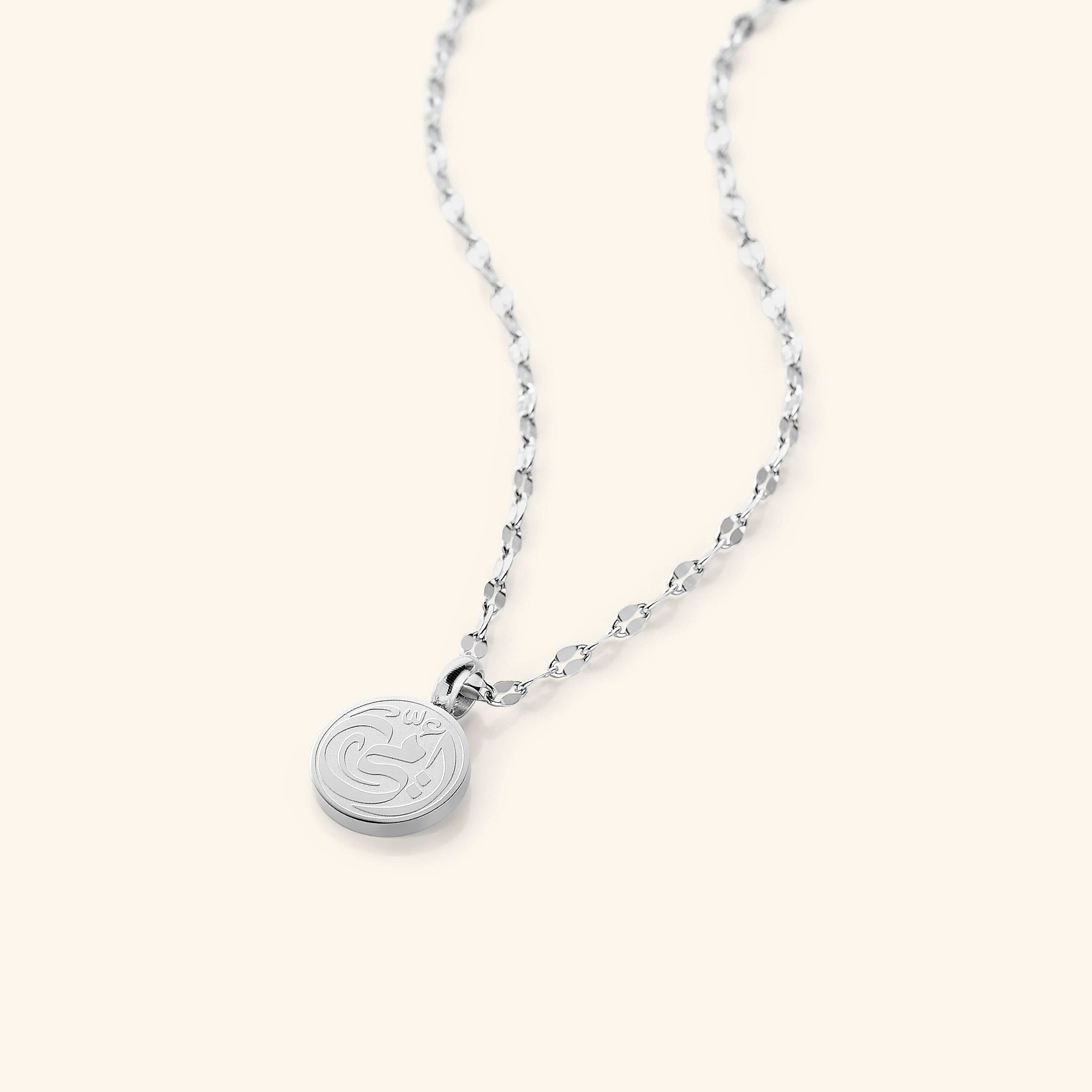 The My Mother Necklace in a polished silver finish, showcasing the round pendant engraved with "أمي" ("Ummi" – My Mother) in graceful Arabic script, hanging from a sleek silver Flutter Chain.