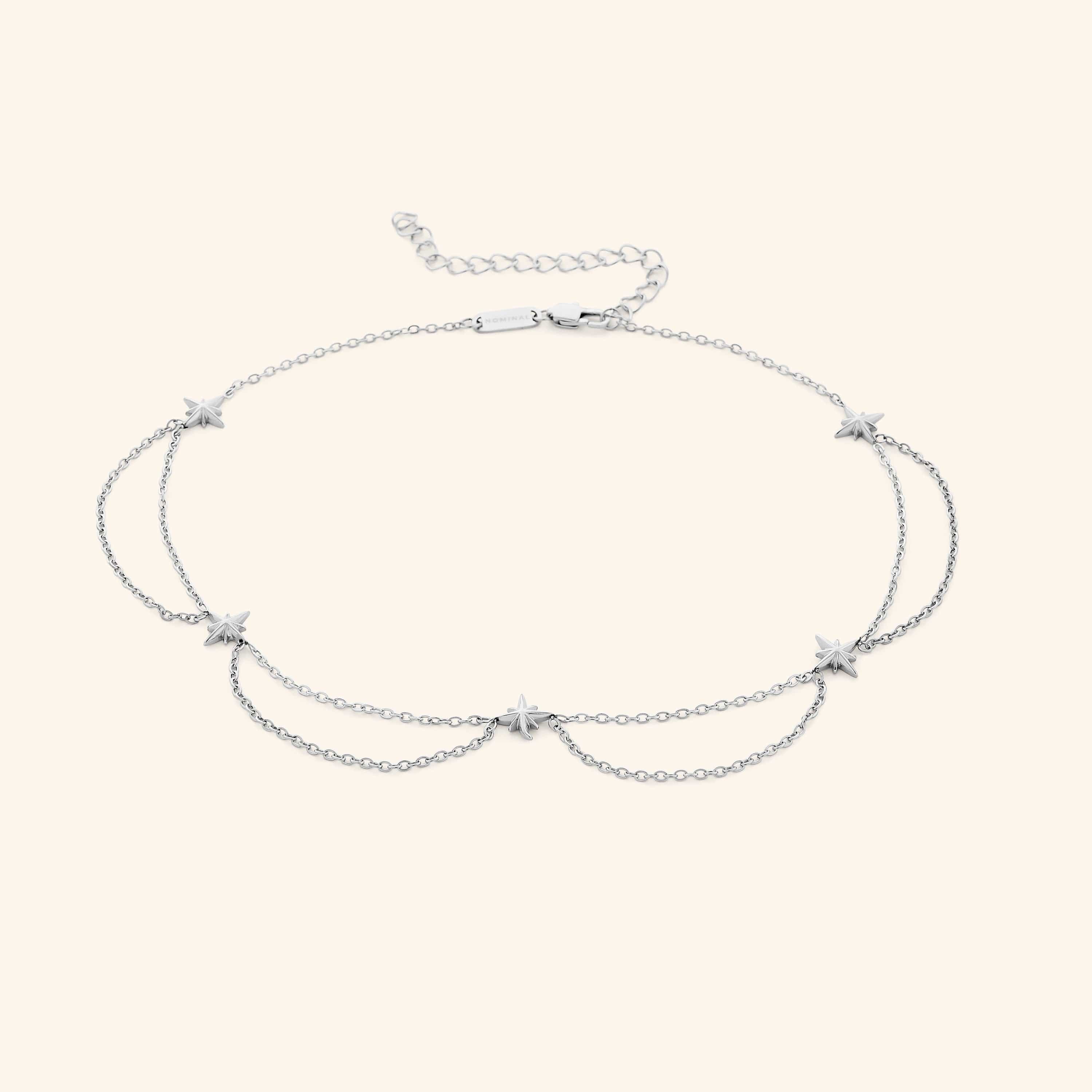 Flat lay of the silver necklace that features north stars all along the chain, drooping chains connecting each one.