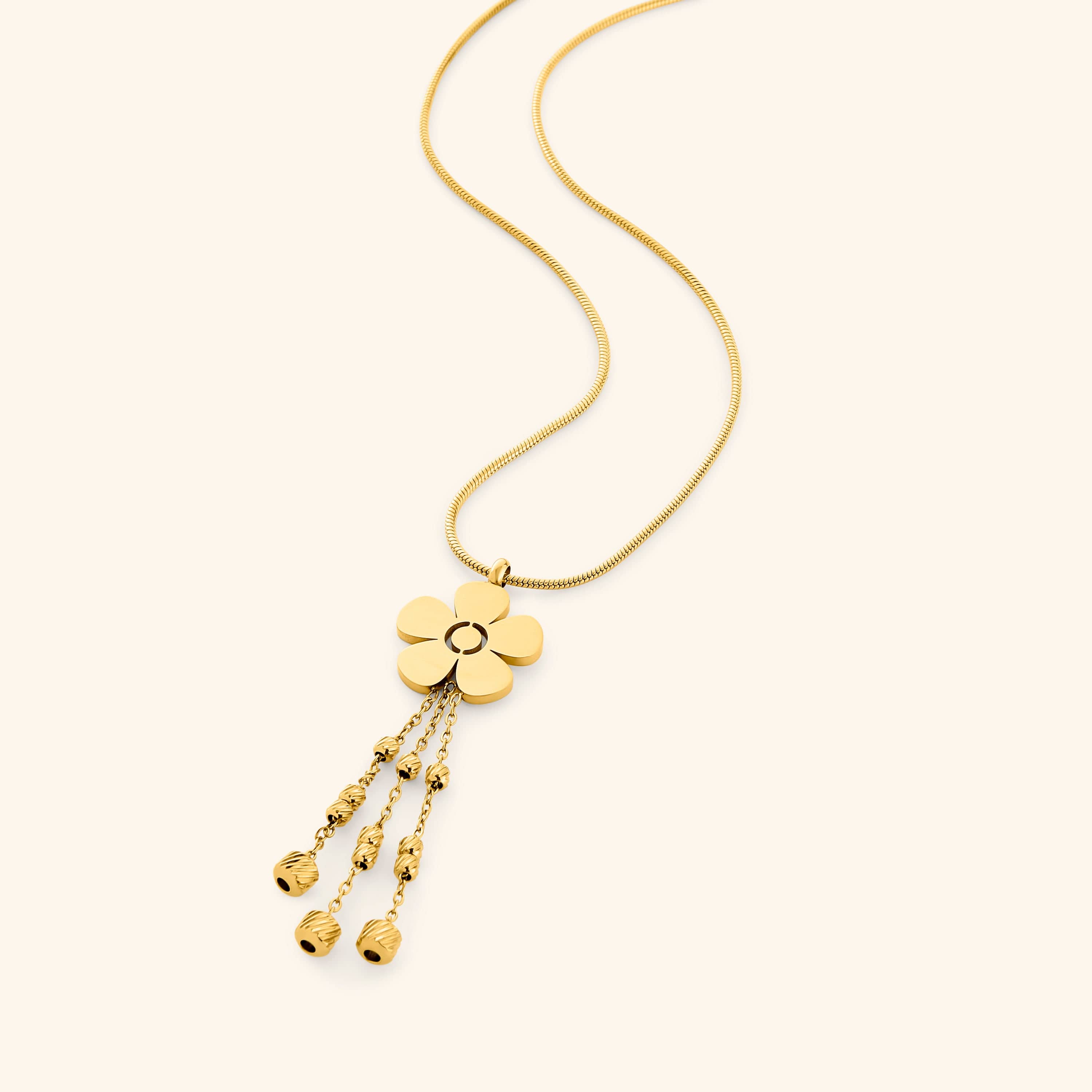 Flat lay of a gold necklace with a five-petal flower pendant, featuring three dangling chains with textured gold beads at the ends.