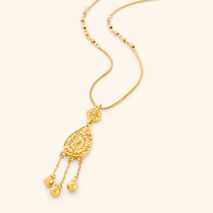 A gold plated necklace the features paisley droplet traced with mehndi-inspired florals, suspended from a beaded chain with three spheres hanging beneath like rain on a thin box chain.