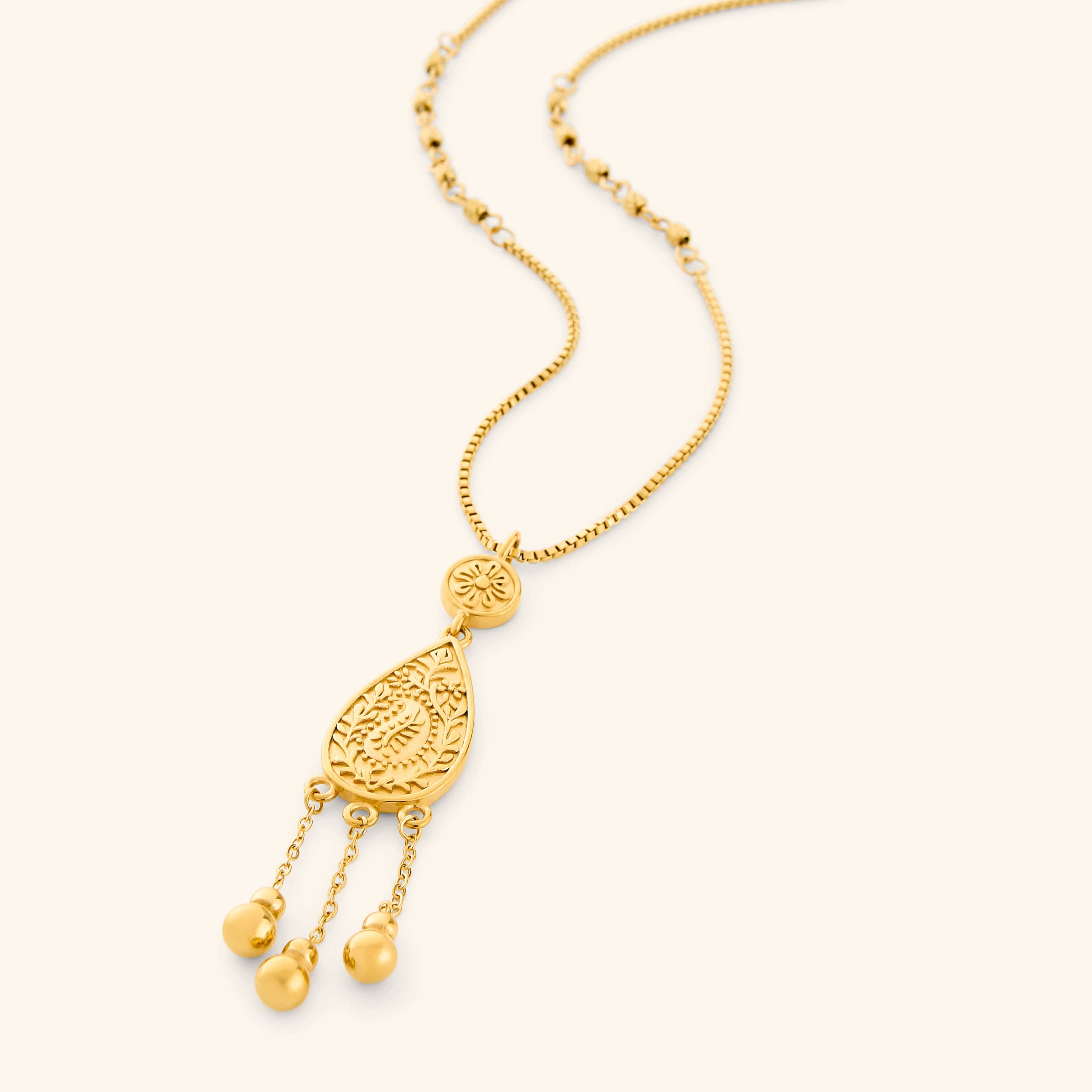 A gold plated necklace the features paisley droplet traced with mehndi-inspired florals, suspended from a beaded chain with three spheres hanging beneath like rain on a thin box chain.