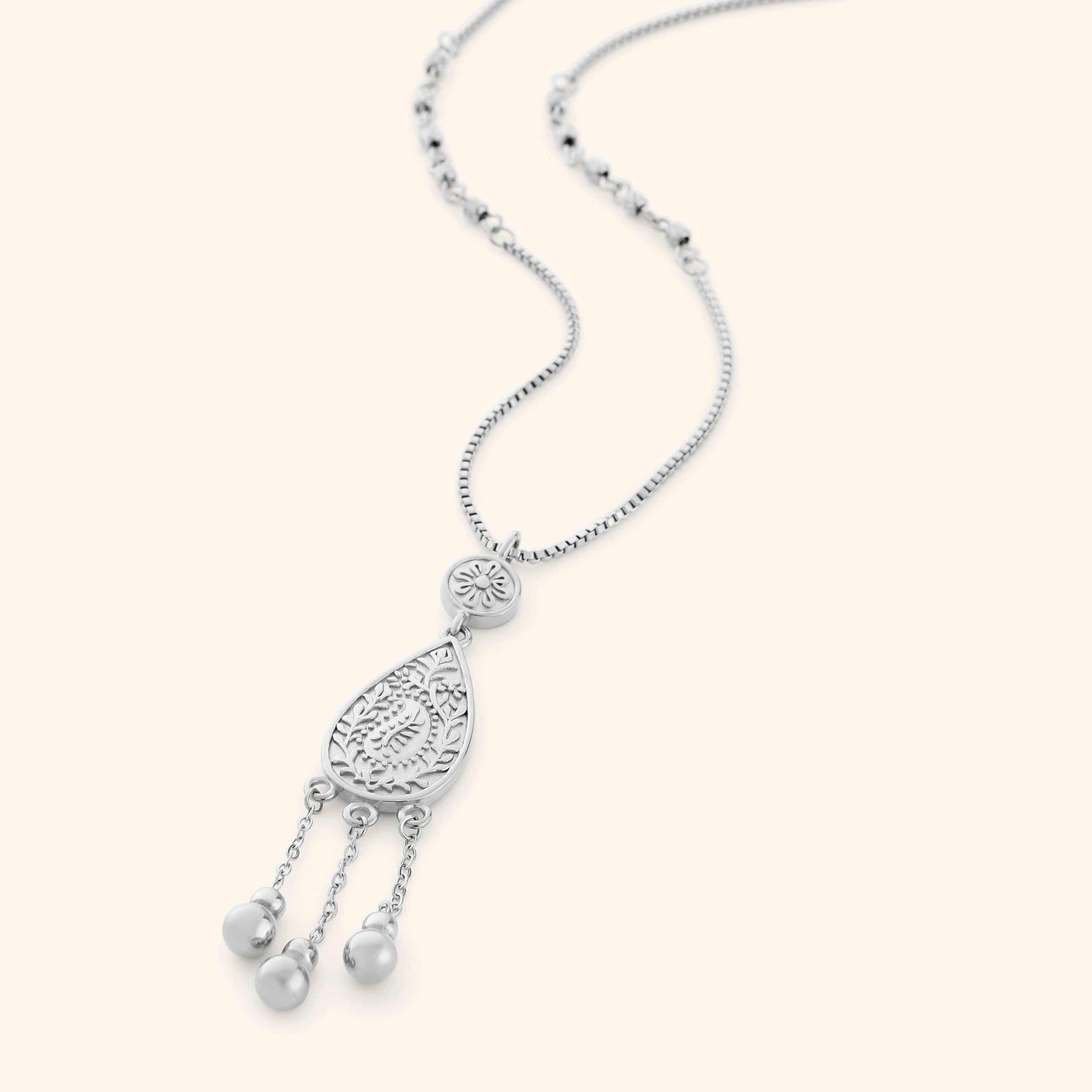 A silver necklace the features paisley droplet traced with mehndi-inspired florals, suspended from a beaded chain with three spheres hanging beneath like rain on a thin box chain.