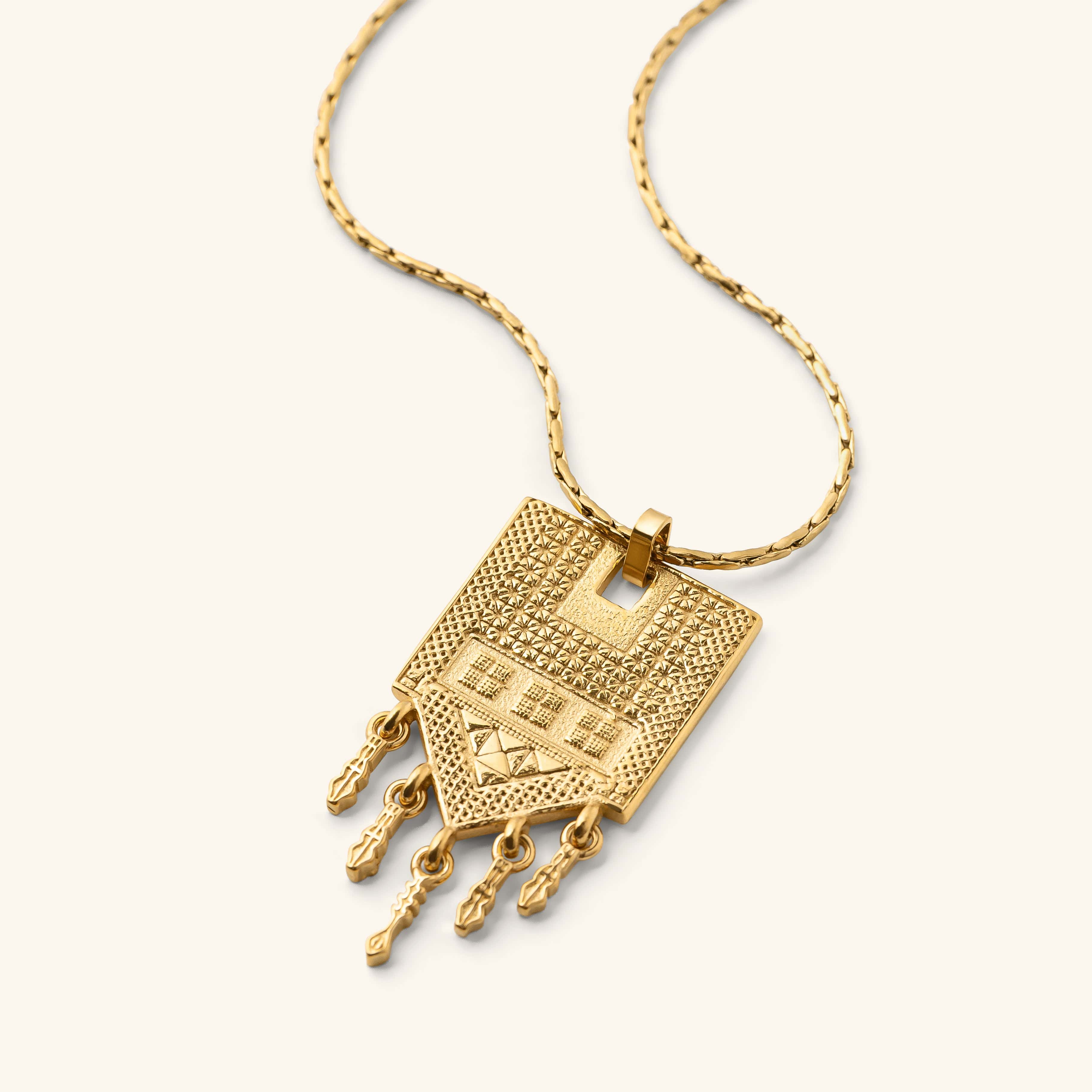 Raining Tatreez Necklace in gold, featuring a pendant with raised Tatreez patterns and five dangling charms, photographed against a neutral background.
