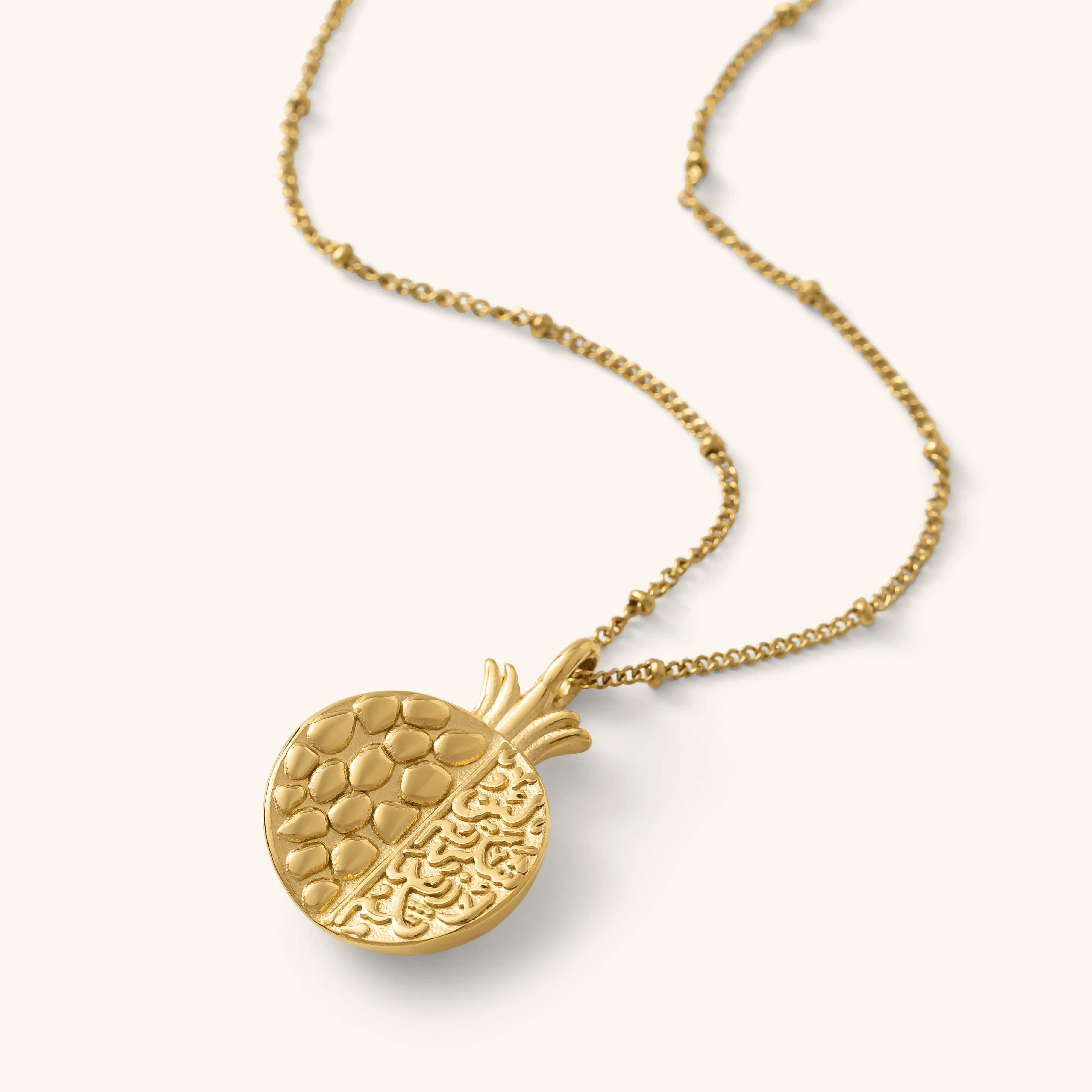 Seeds of Gratitude Necklace in gold featuring a pomegranate-shaped pendant with engraved seeds on one half and Arabic calligraphy on the other.