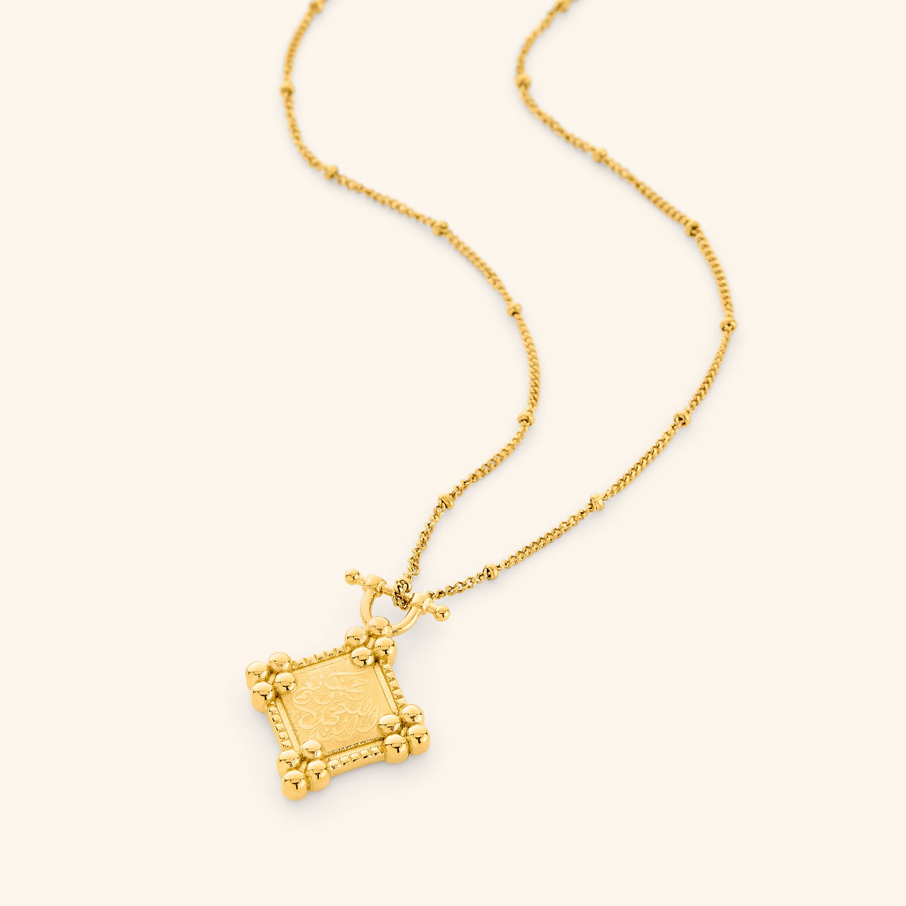 Photo of a necklace with 18k gold plated diamond-shaped plaque stamped with حَسْبُنَا اللَّهُ وَنِعْمَ الْوَكِيلُ (Hasbunallahu wa ni'mal wakeel). "Allah is sufficient for us, and He is the best Disposer of affairs." framed in beaded borders on a thin dotted chain.