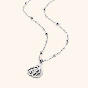 Silver necklace with beaded chain and teardrop-shaped pendant featuring Arabic calligraphy spelling “Sister”, photographed flat against a cream background.