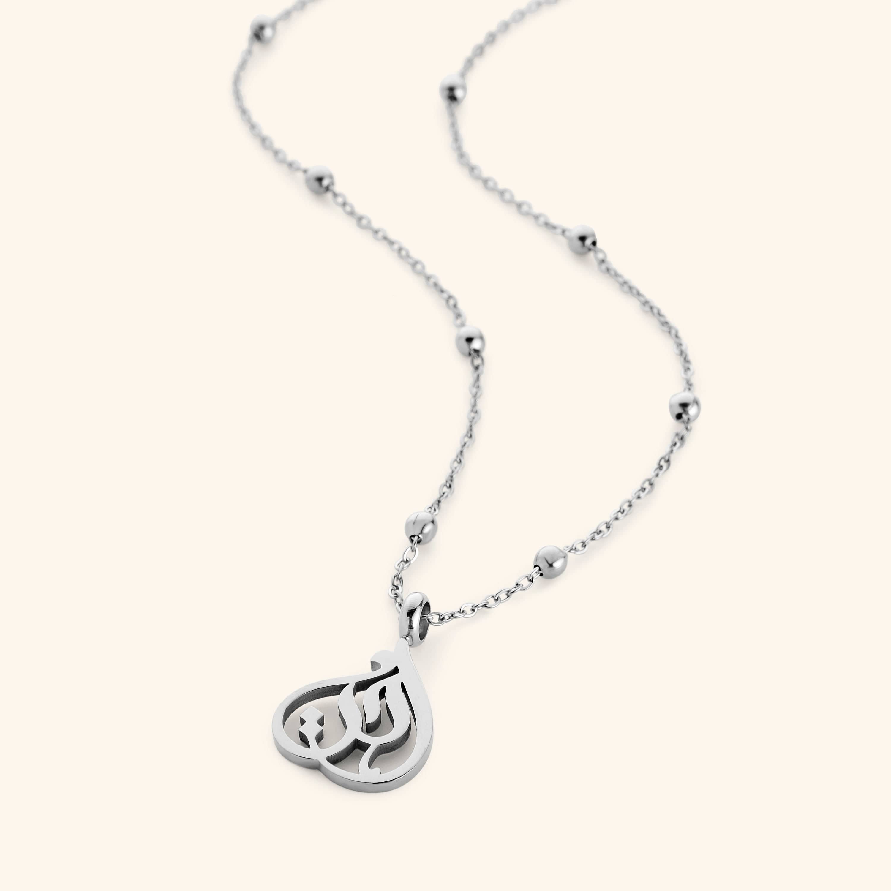 Silver necklace with beaded chain and teardrop-shaped pendant featuring Arabic calligraphy spelling “Sister”, photographed flat against a cream background.