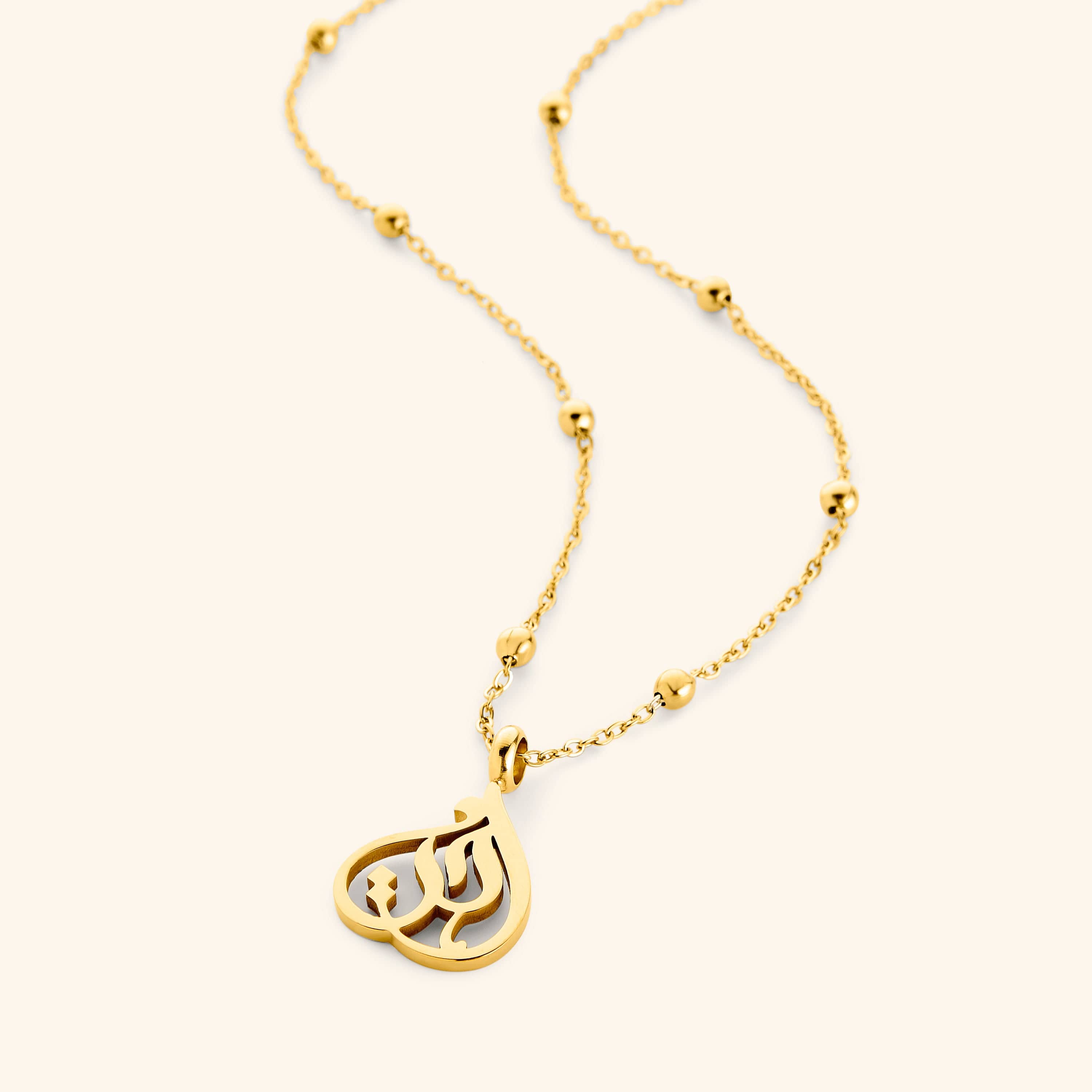 Gold necklace with beaded chain and teardrop-shaped pendant featuring Arabic calligraphy spelling “Sister”, photographed flat against a cream background.