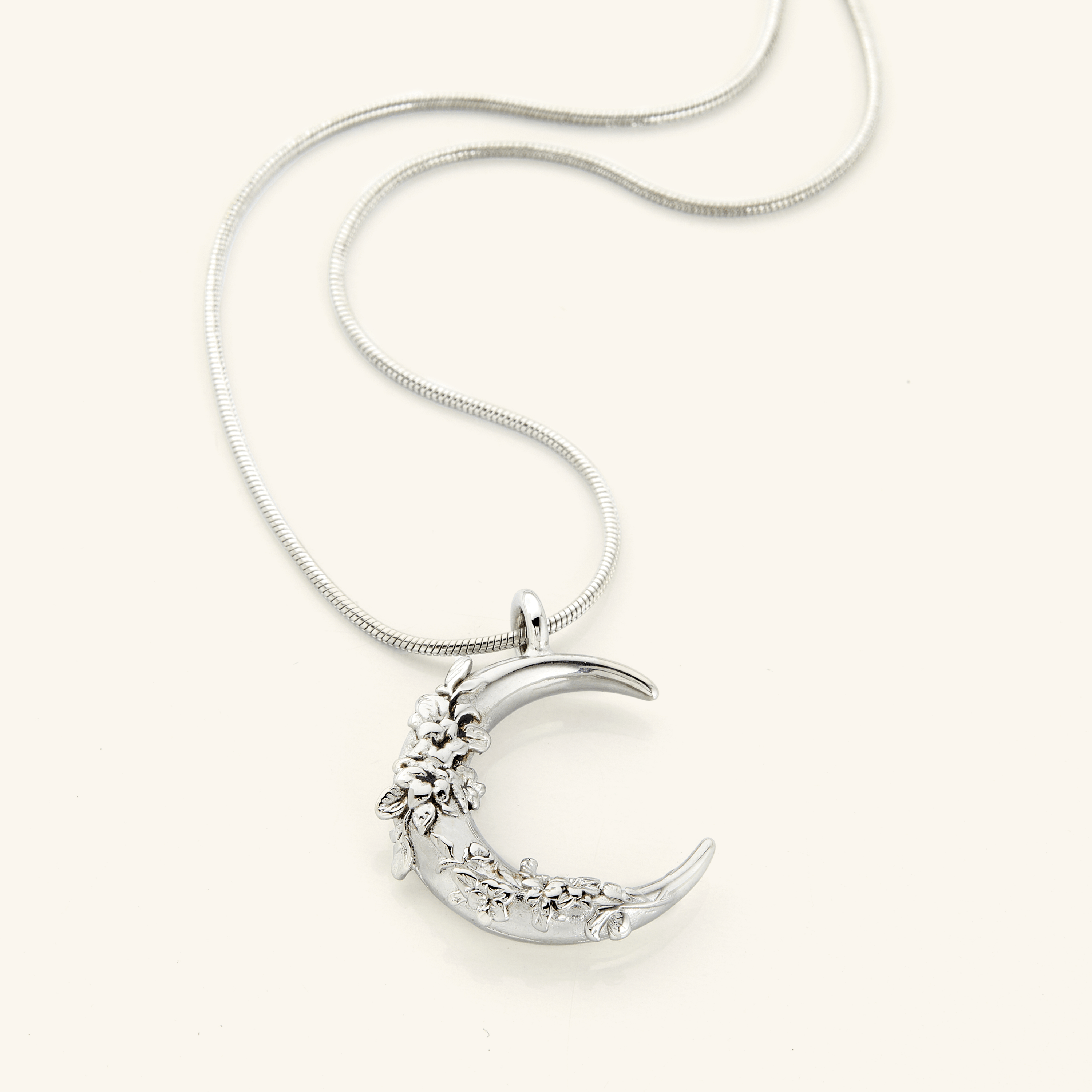 The Jasmine Crescent Necklace in a polished silver finish, showcasing a crescent pendant with detailed jasmine vine engravings, hanging from the Harmony Chain.