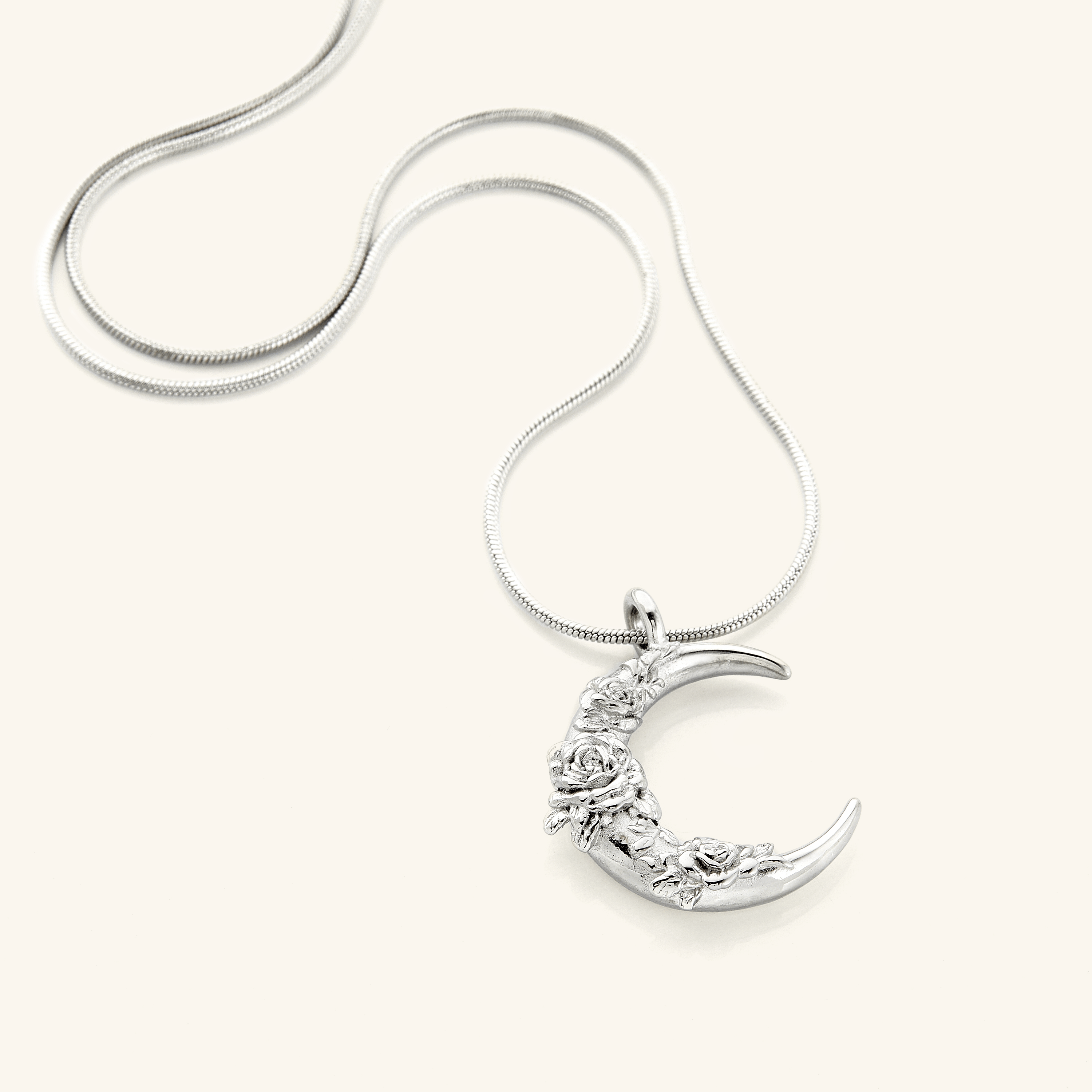 The Damask Rose Crescent Necklace in a polished silver finish, showcasing a crescent moon pendant with detailed damask rose engravings, hanging from a slender silver chain.