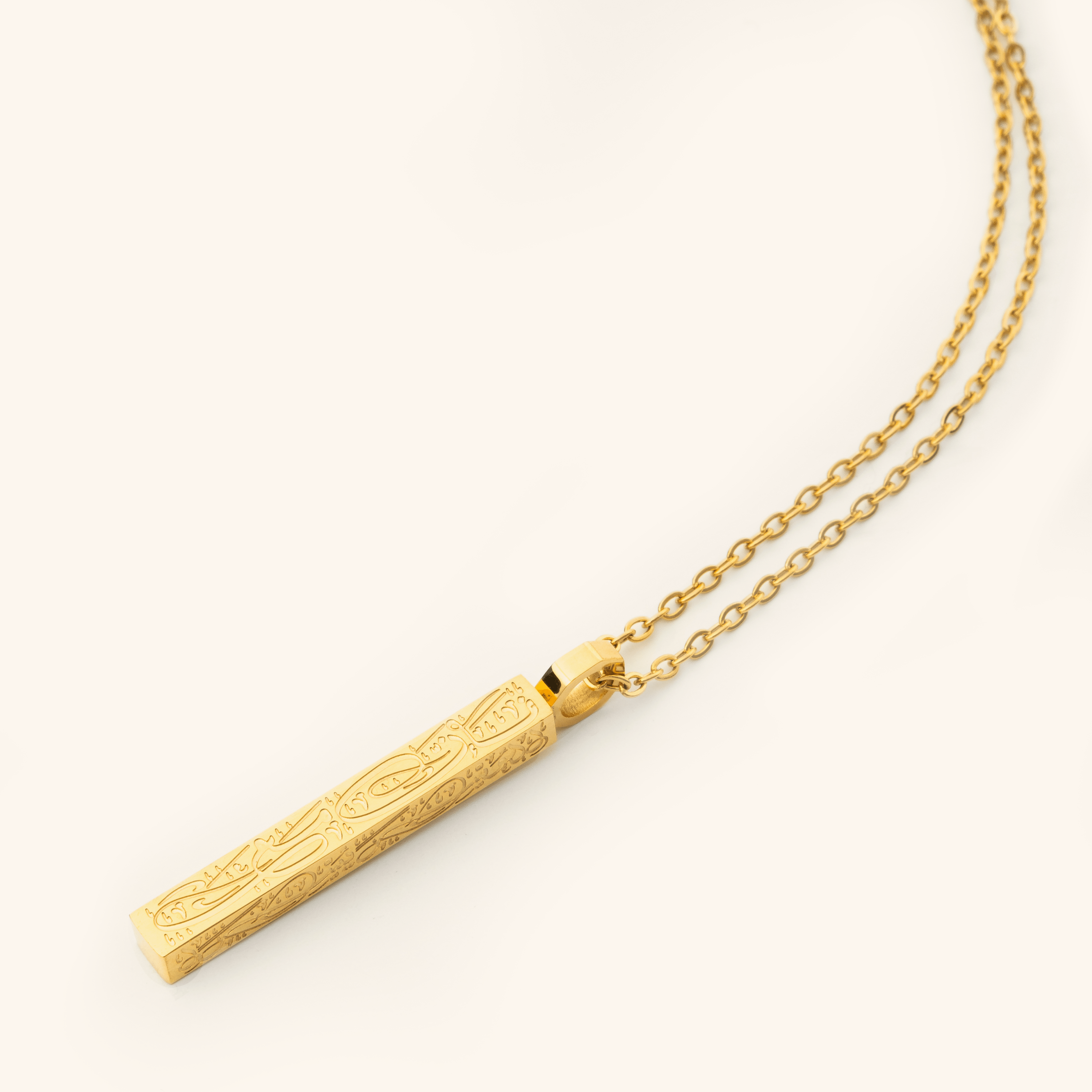 Photo of an 18k gold plated necklace that features the Arabic Calligraphy of  'with every hardship comes ease' that is engraved intricately all along this timeless bar pendant. 