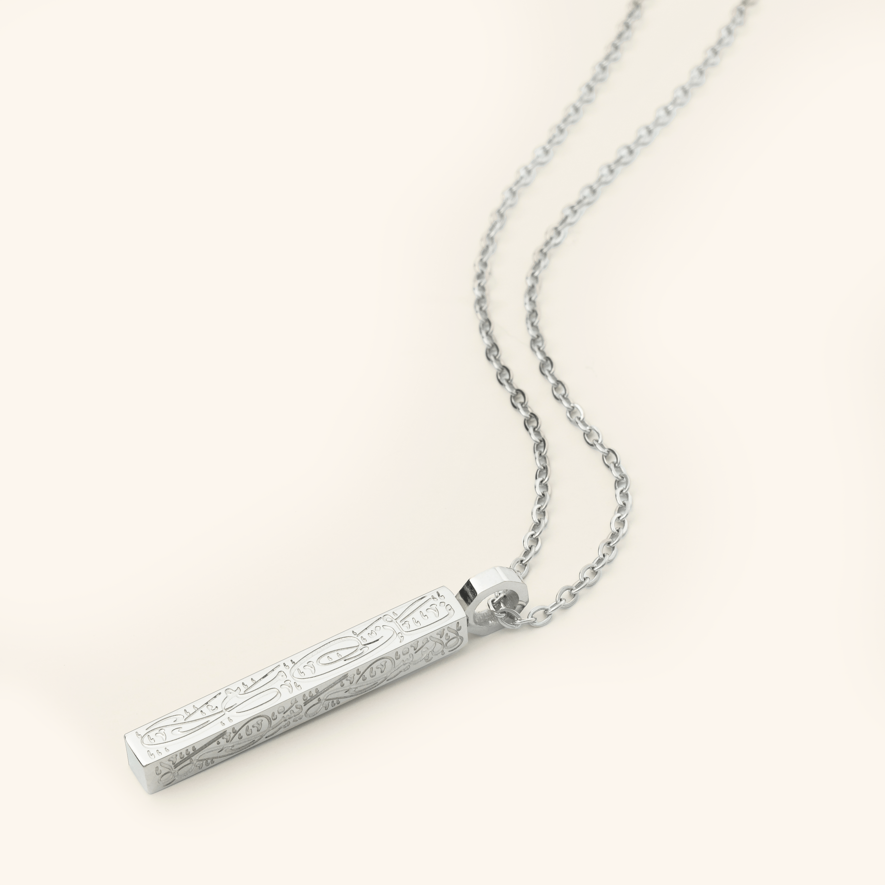 Photo of a silver necklace that features the Arabic Calligraphy of  'with every hardship comes ease' that is engraved intricately all along this timeless bar pendant. 