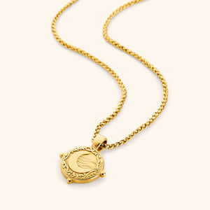 Gold necklace with a round pendant featuring the engraved phrase 'What you seek is seeking you' in Arabic calligraphy. The design includes a raised crescent moon and a flowing motif, framed with vine detailing and three small bead accents around the border. 